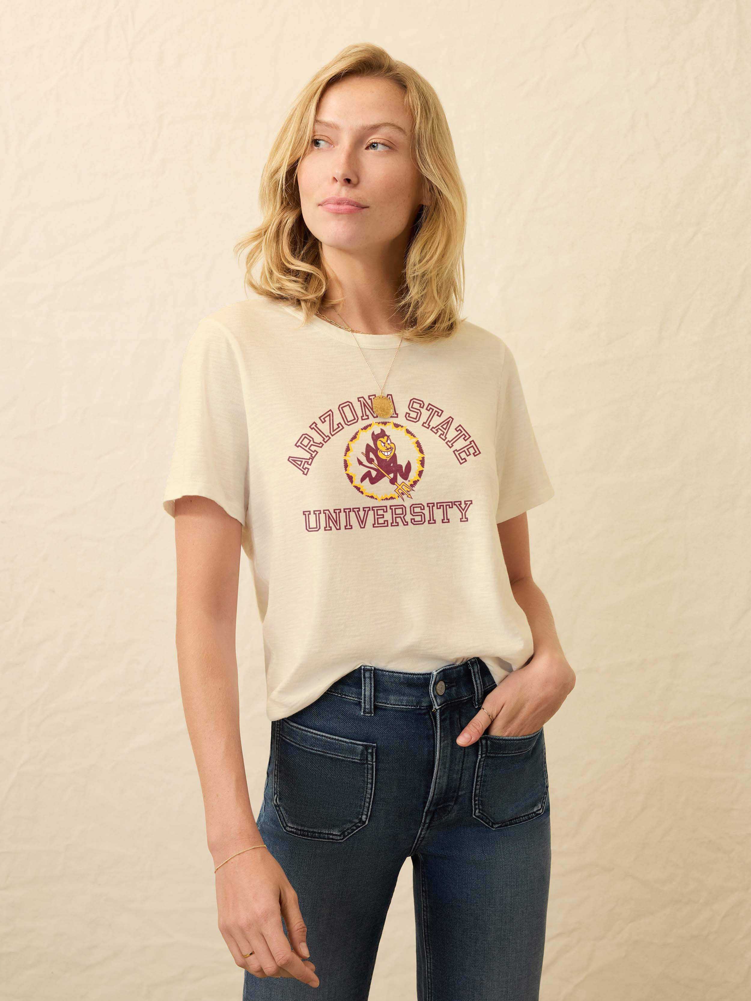Woman wearing a pale yellow t-shirt with Arizona State University graphic on the center front against a beige background