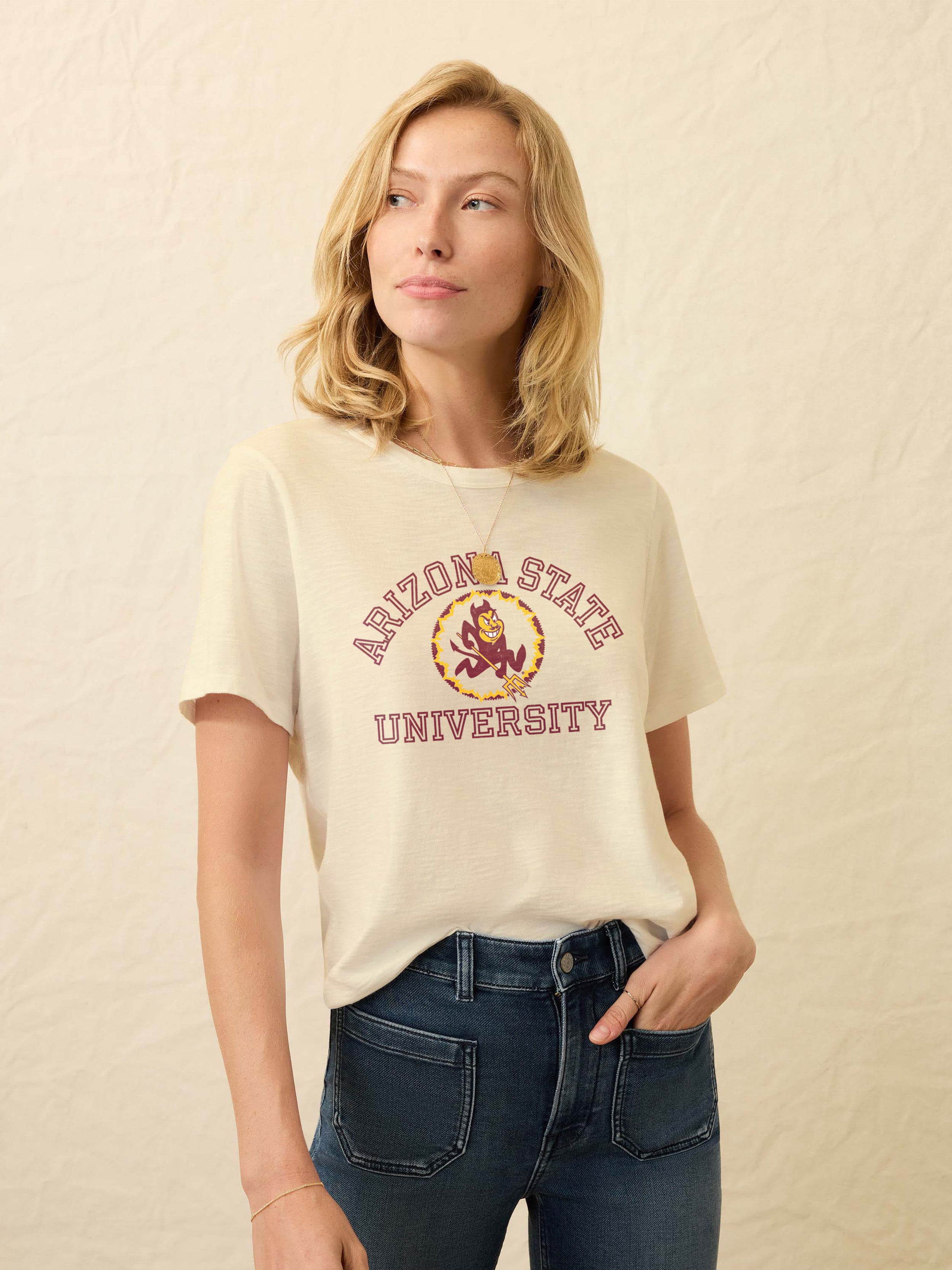 Woman wearing a pale yellow t-shirt with Arizona State University graphic on the center front against a beige background