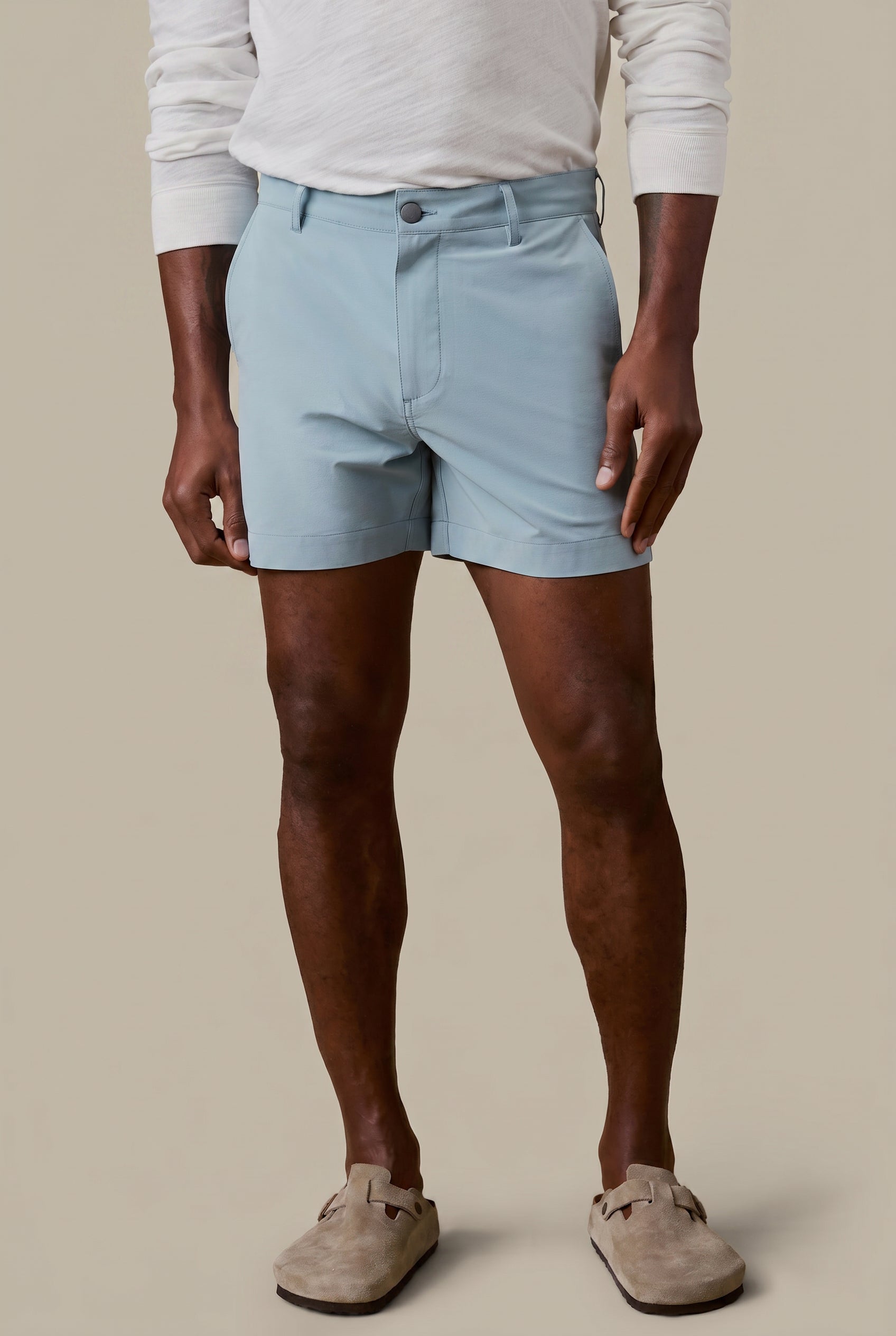 Man wearing light blue shorts and a white long-sleeve shirt on a beige background