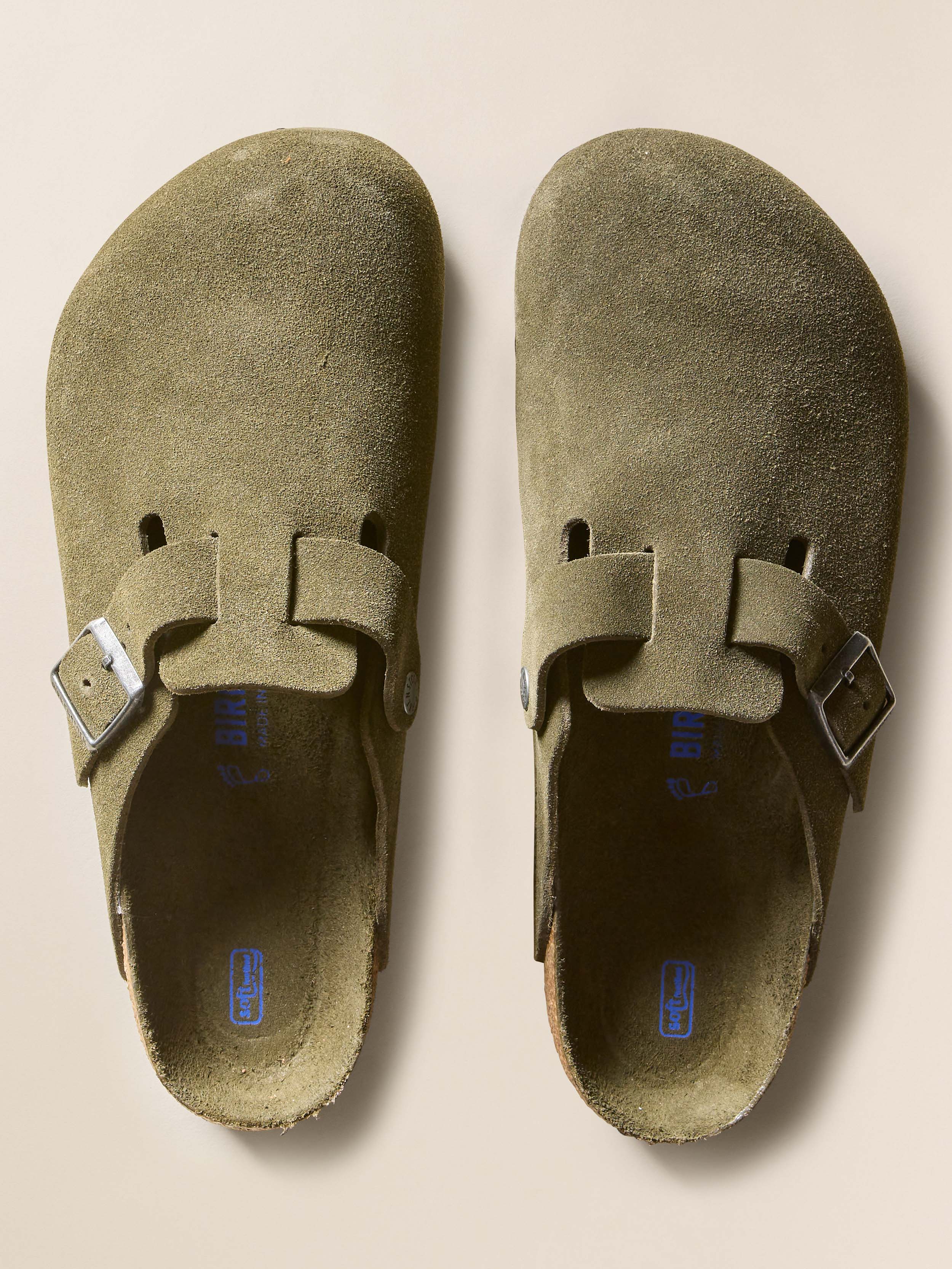 Pair of green suede Birkenstock clogs with buckles on a beige background