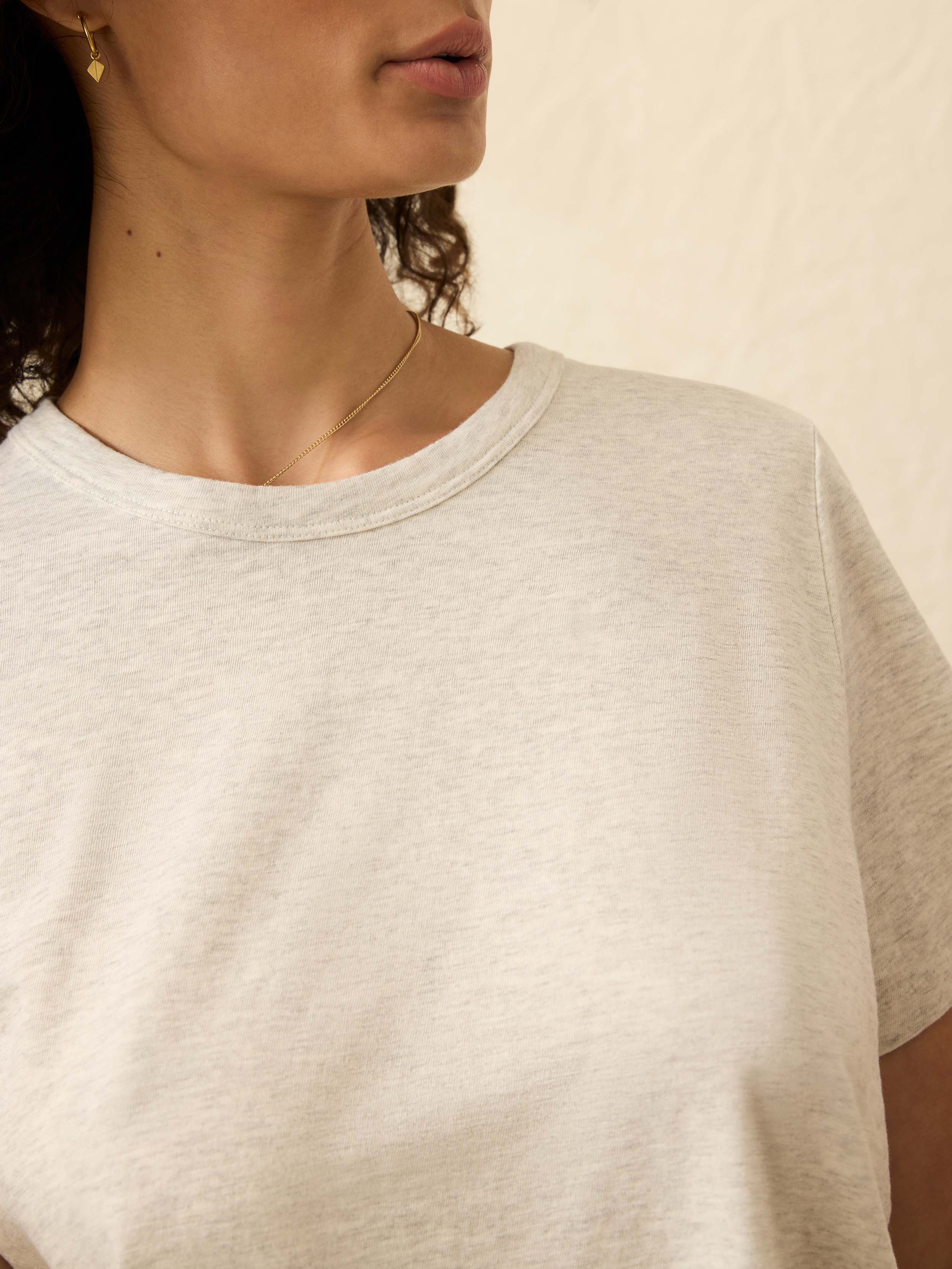 Close-up of a person wearing a light heather gray t-shirt against a neutral background
