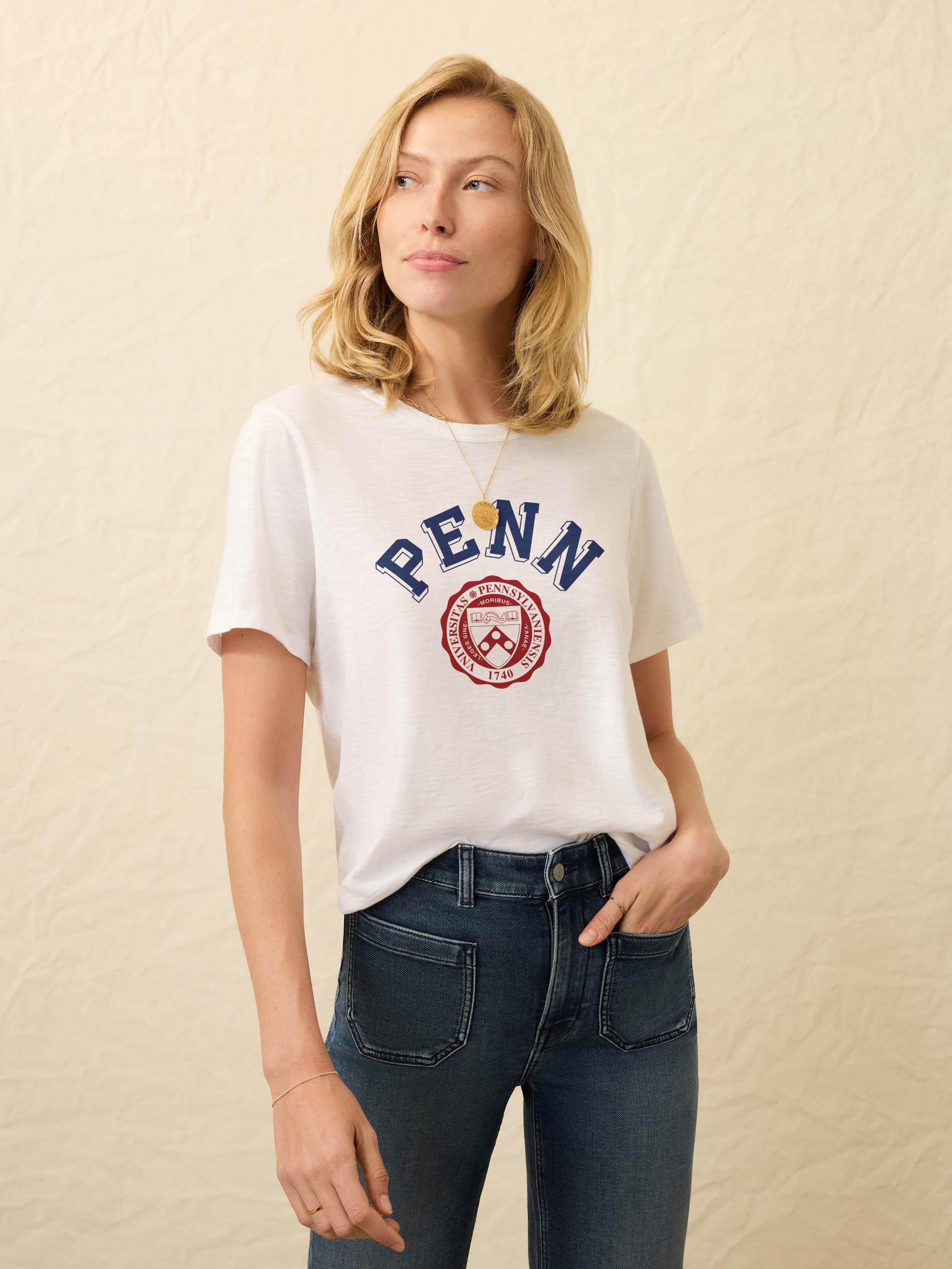 Woman wearing white short sleeve t-shirt with University of Pennsylvania graphic on the front against a beige background