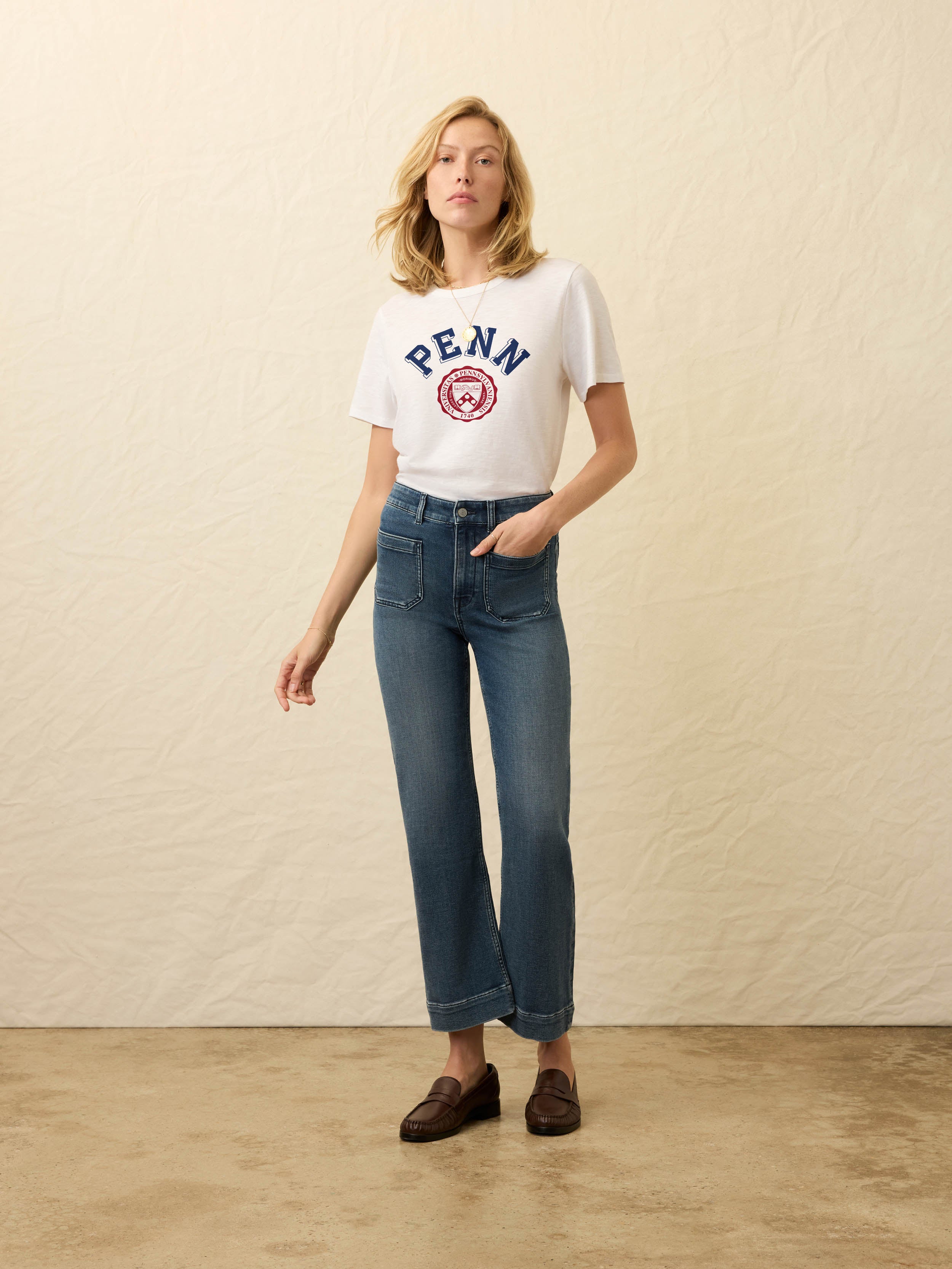 Woman wearing white short sleeve t-shirt with University of Pennsylvania graphic on the front against a beige background