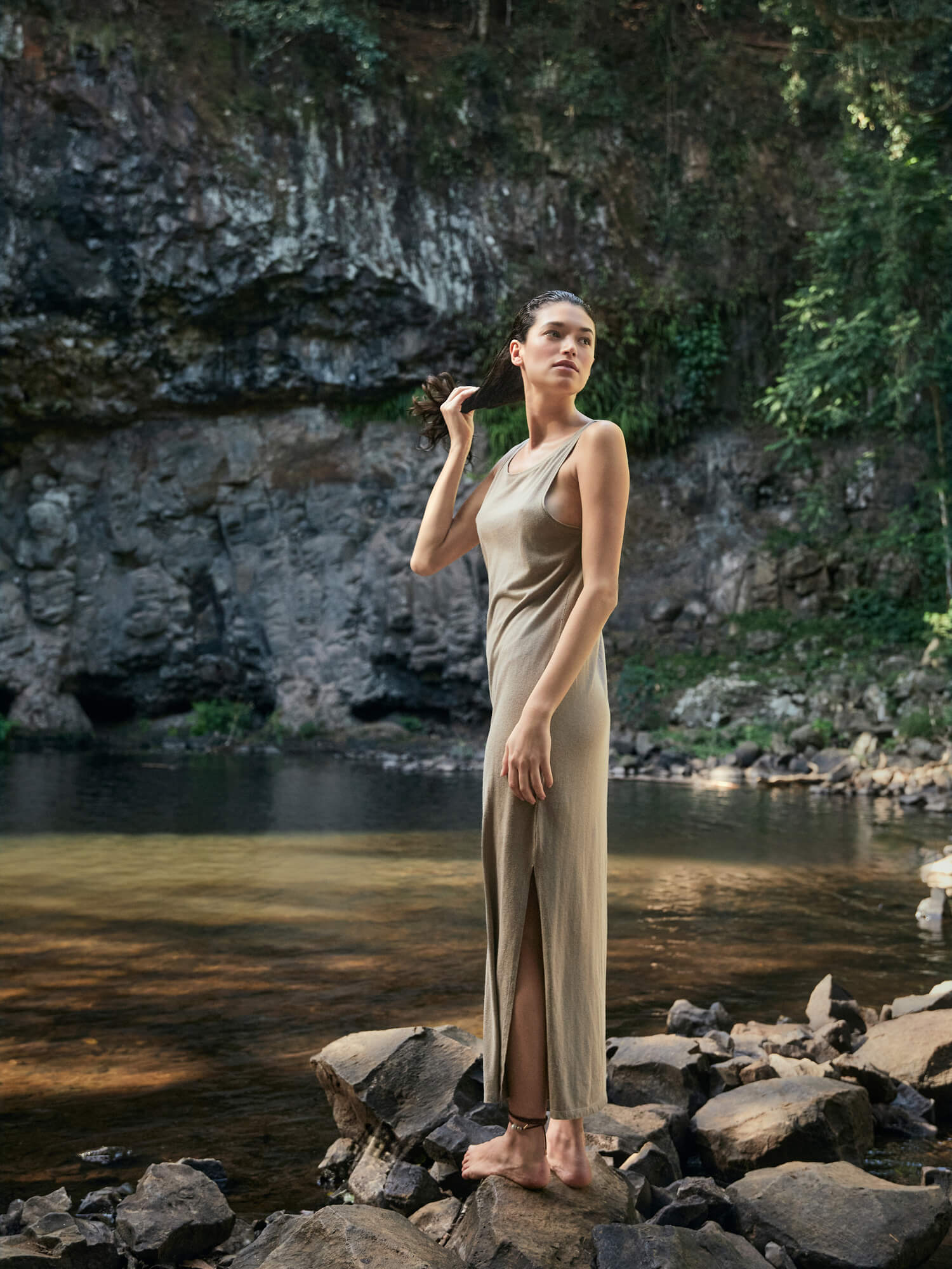 Woman in a flowing dress standing by a river with rocky cliffs in the background