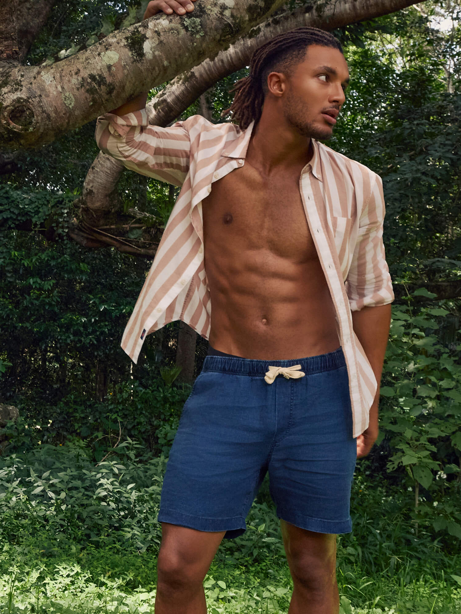 Man in blue linen shorts and a striped shirt standing in a forest