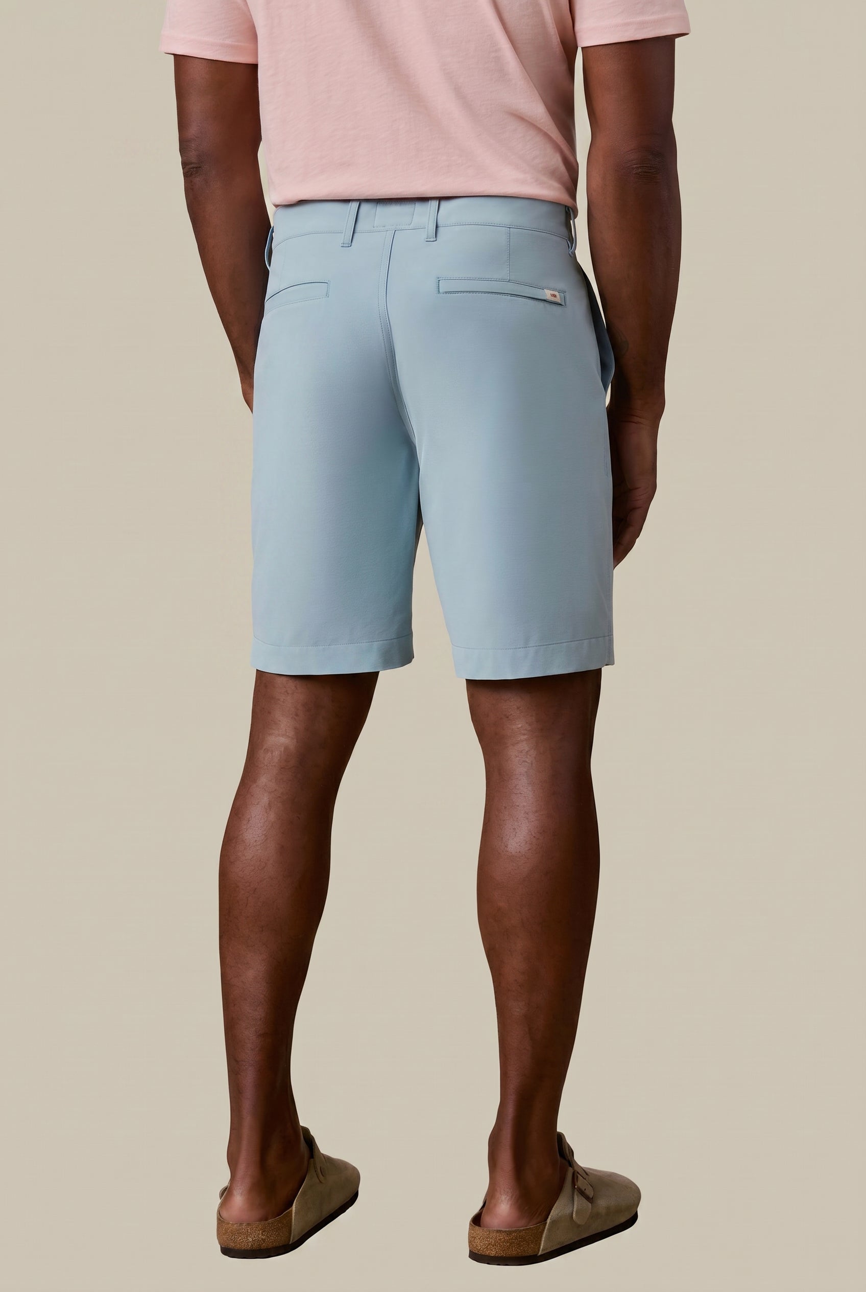 Man wearing light blue shorts and a pink shirt on a beige background