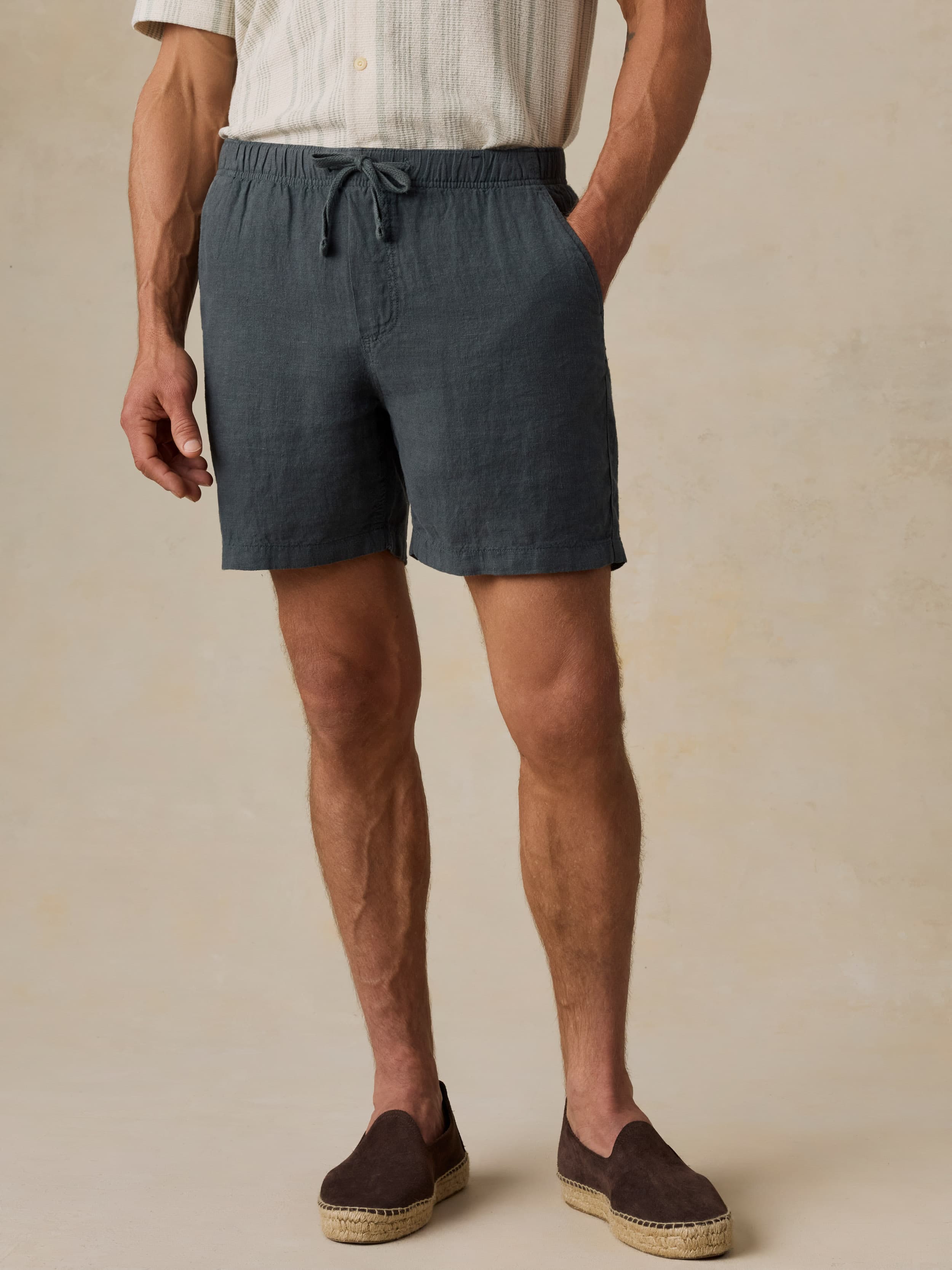 Man wearing a light-colored shirt and black linen shorts against a beige background