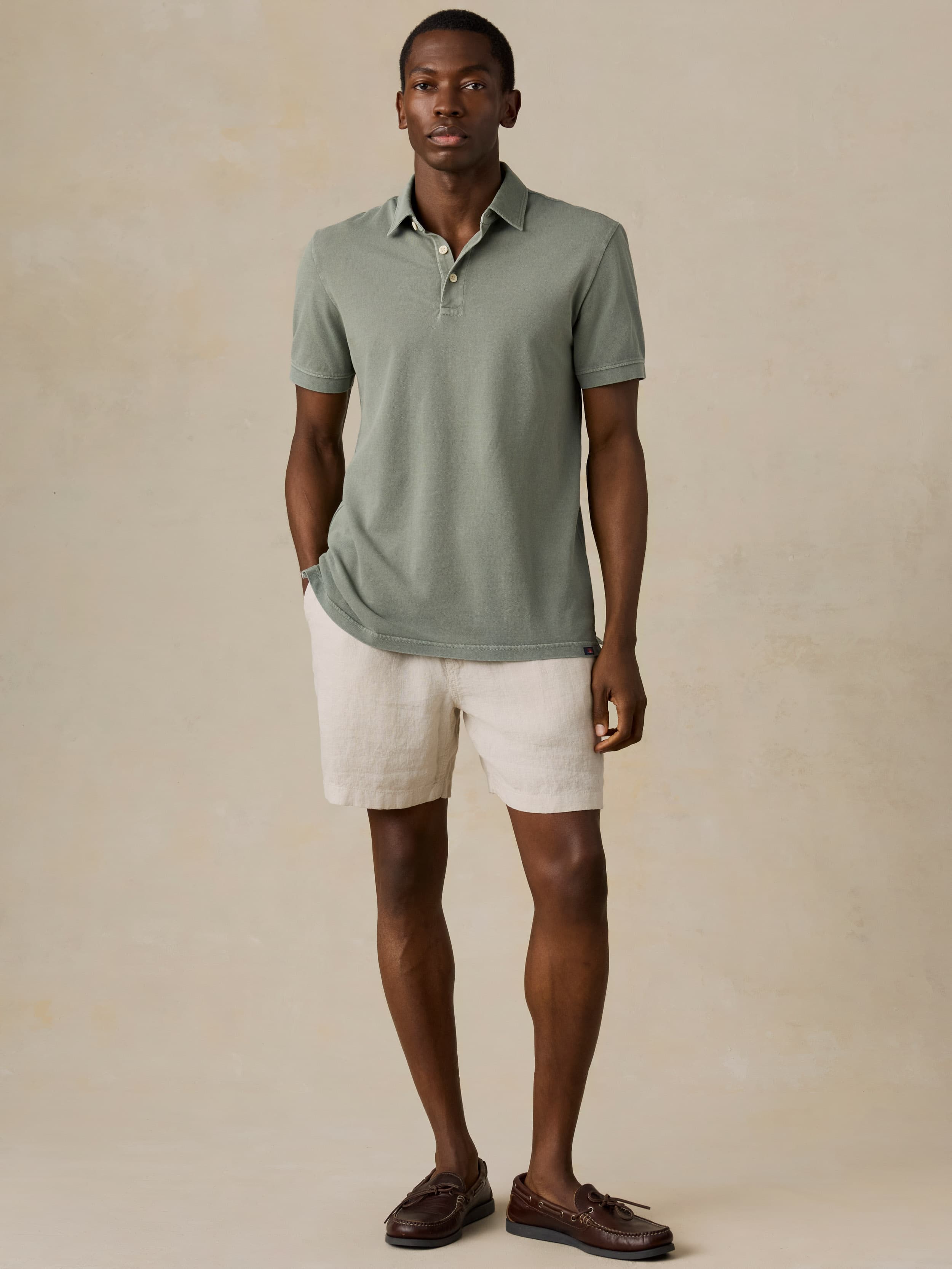 Man wearing a light green polo shirt and beige linen shorts against a beige background
