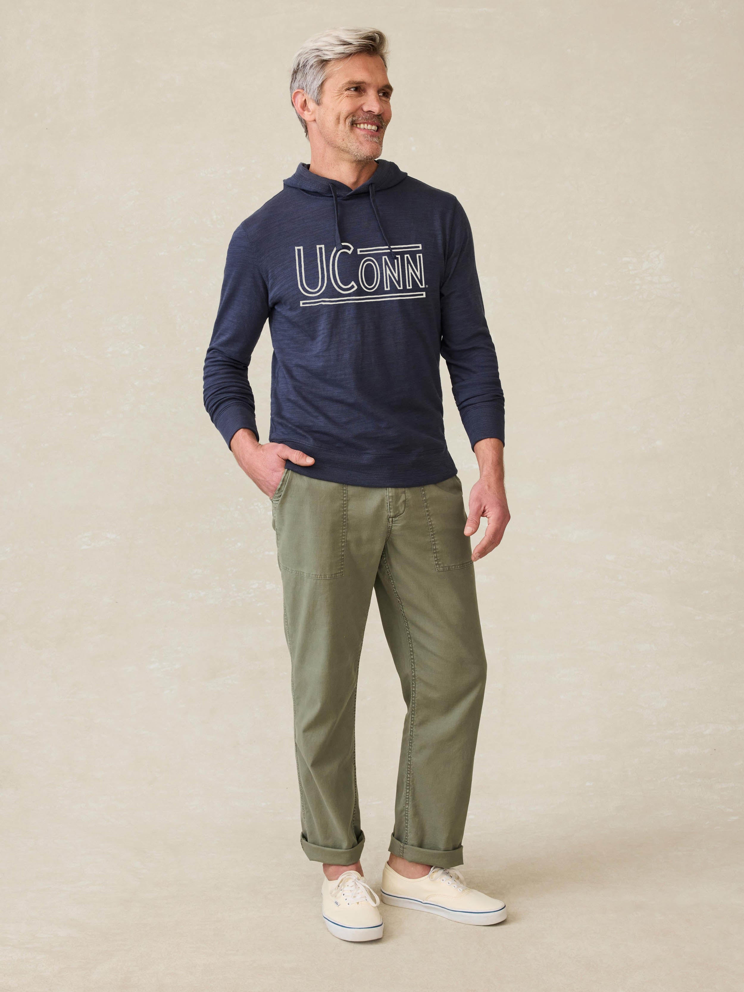 Man is wearing a navy blue hoodie with UCONN graphic at the center front against a beige background