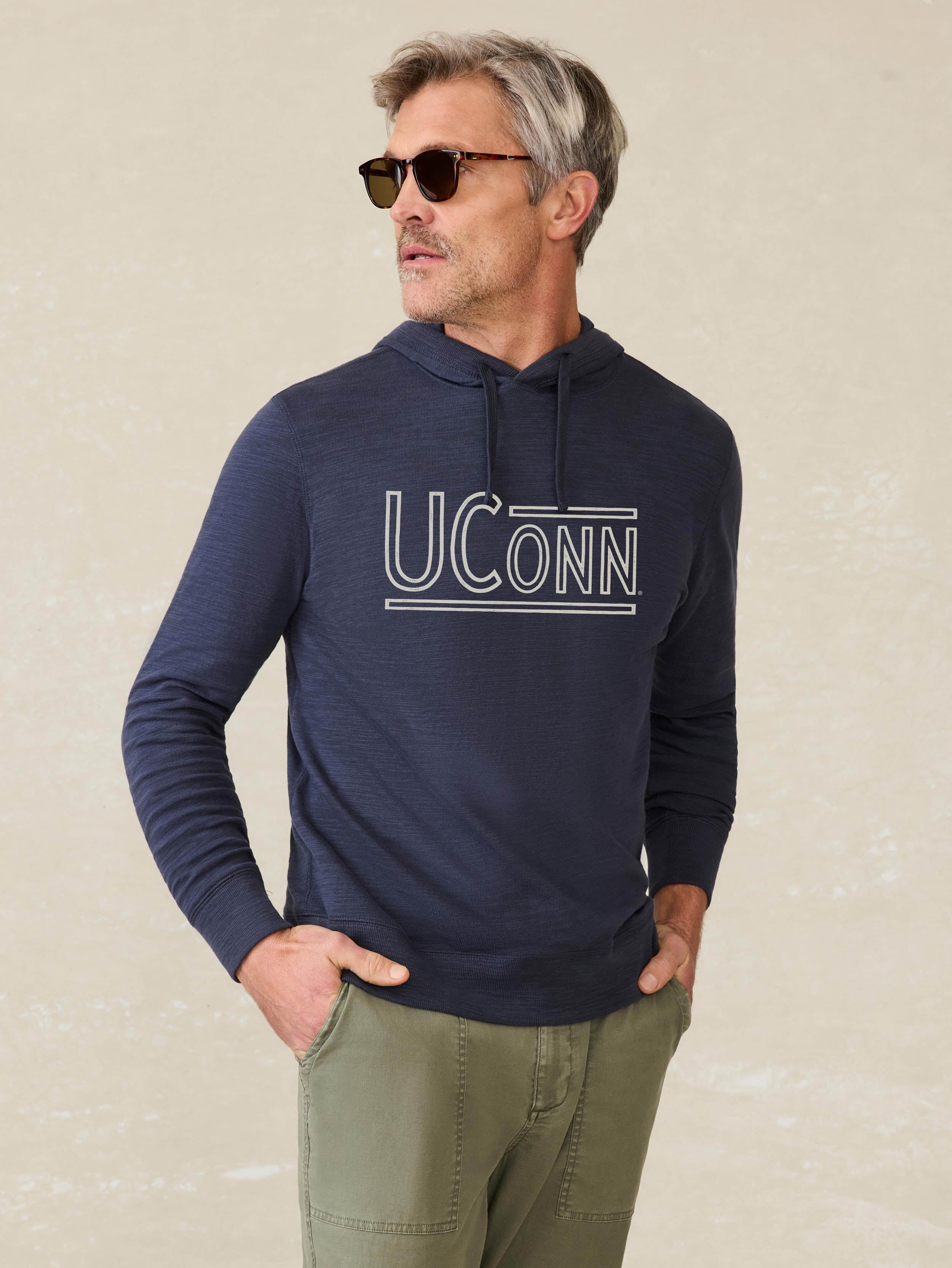 Man is wearing a navy blue hoodie with UCONN graphic at the center front against a beige background