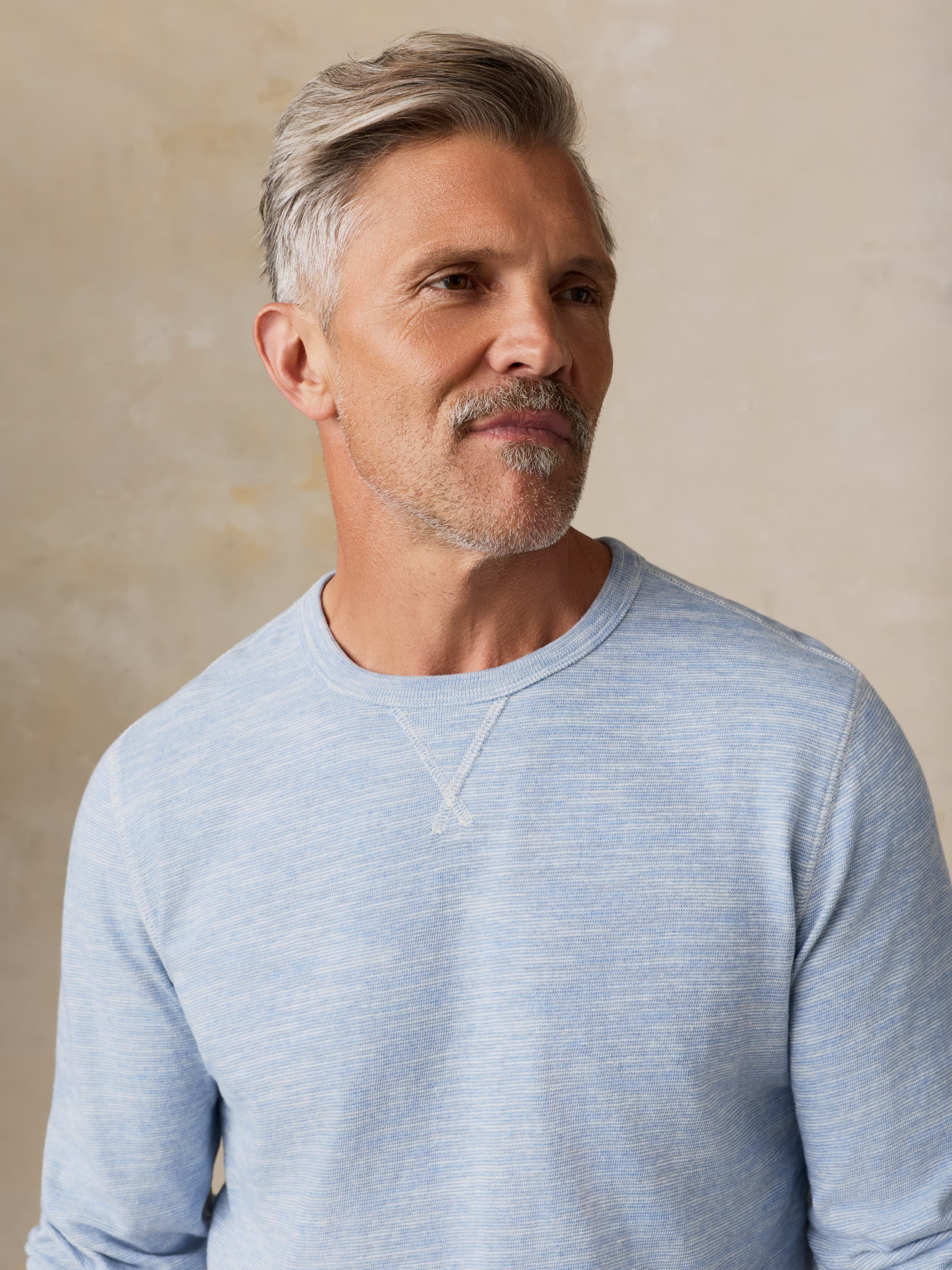 Man wearing a light blue crewneck against a beige background