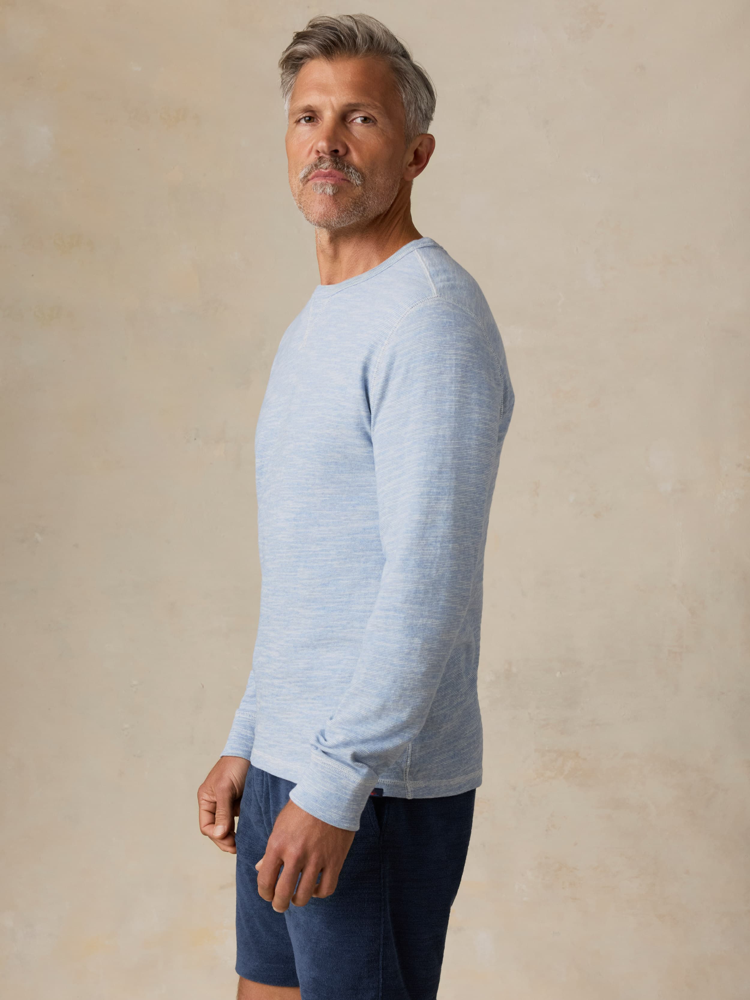 Man wearing a light blue crewneck and navy shorts against a beige background