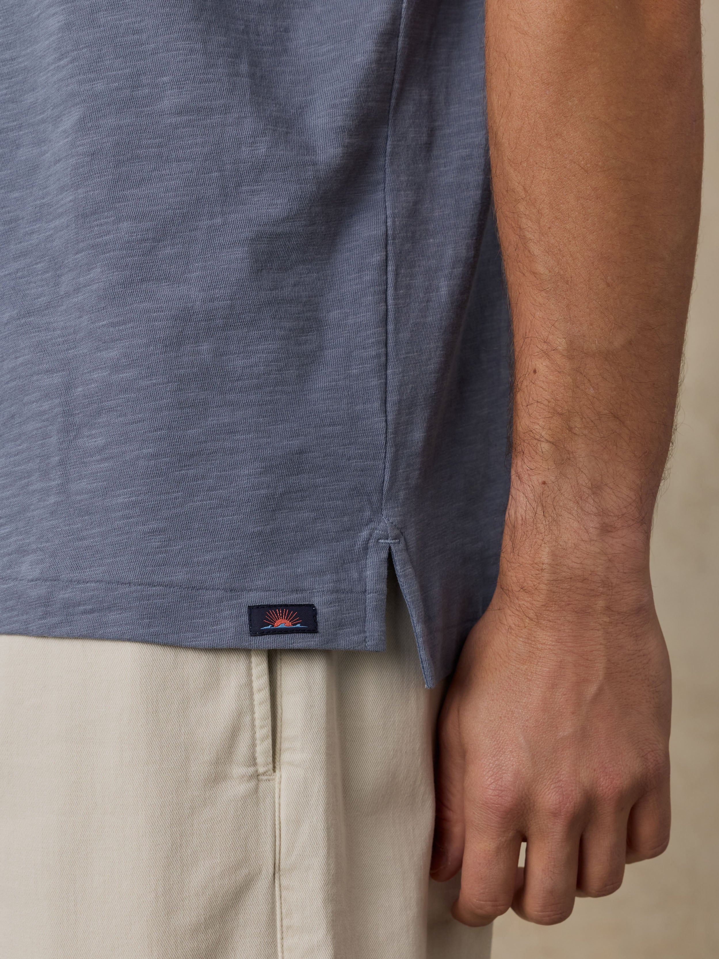 Close-up of a man wearing a blue polo shirt with a Faherty brand logo and beige pants on a neutral background