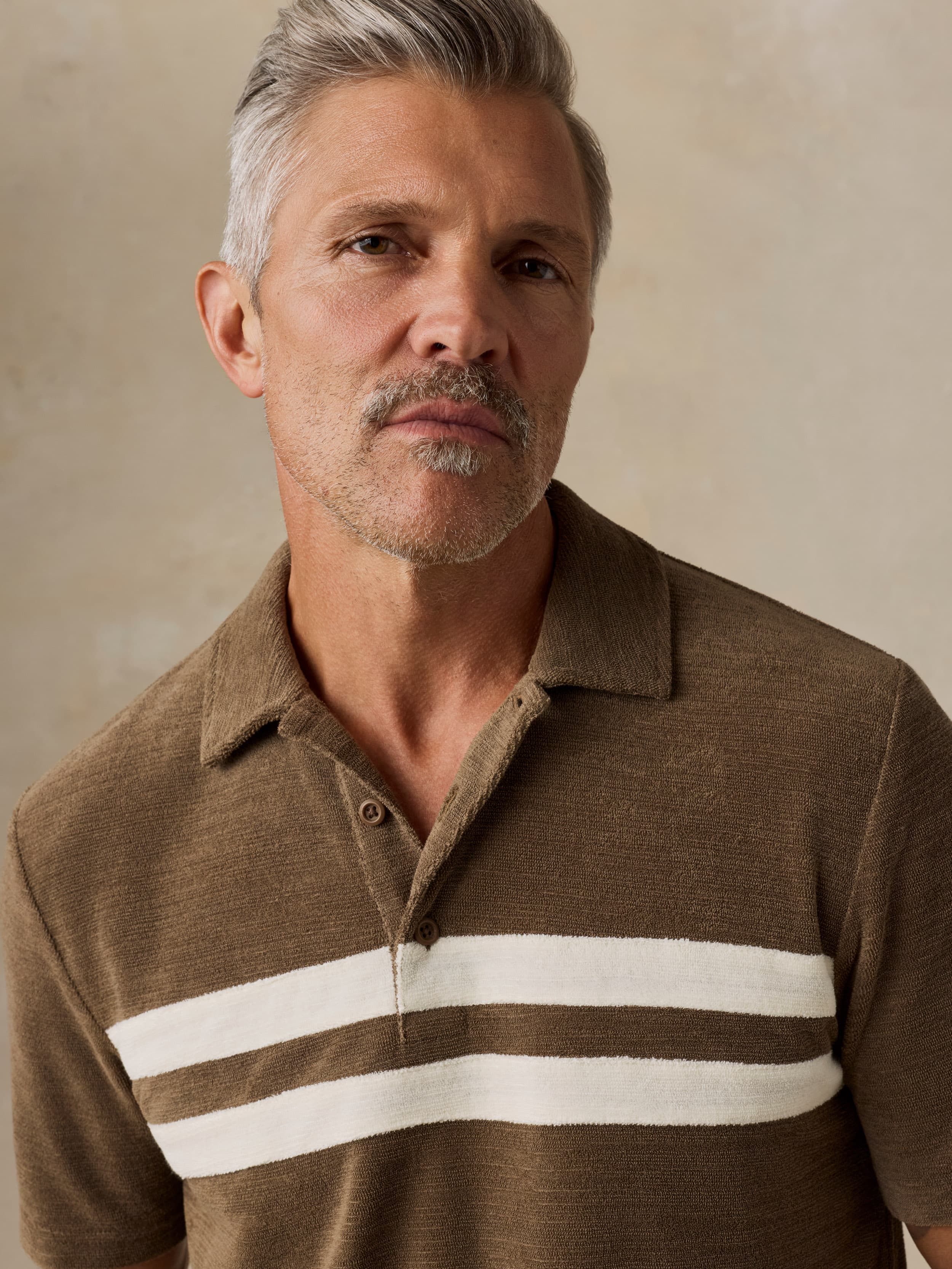 Man wearing a brown polo shirt with white stripes against a beige background