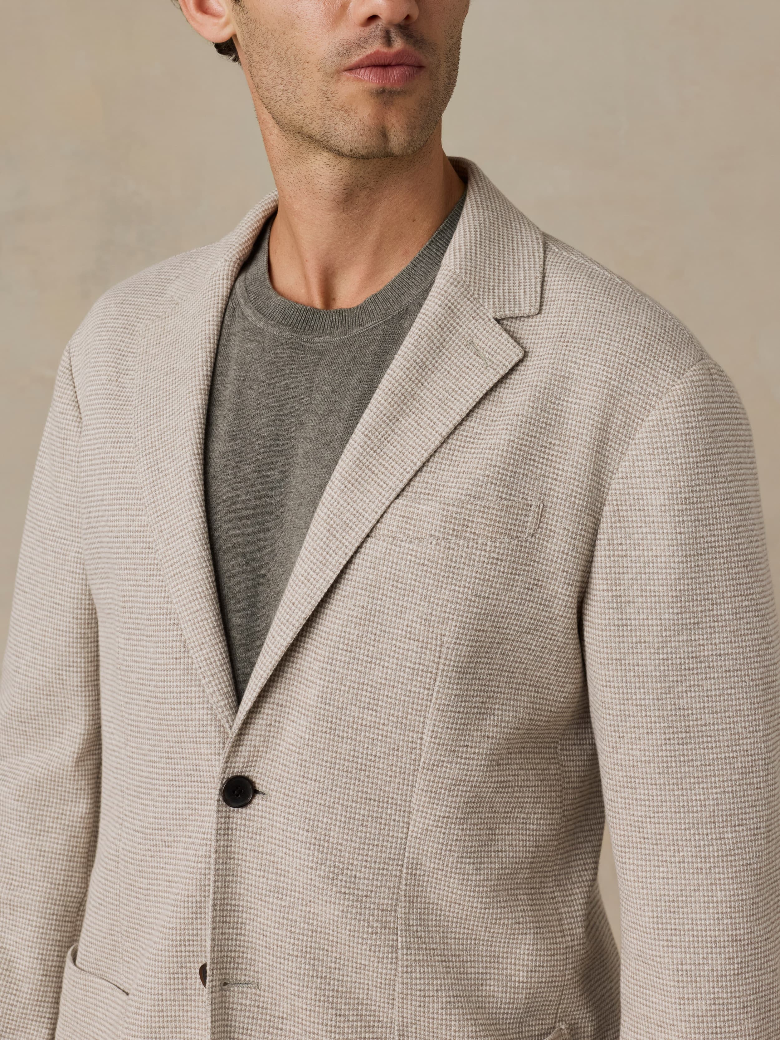 Man wearing a beige blazer over a gray shirt against a beige background