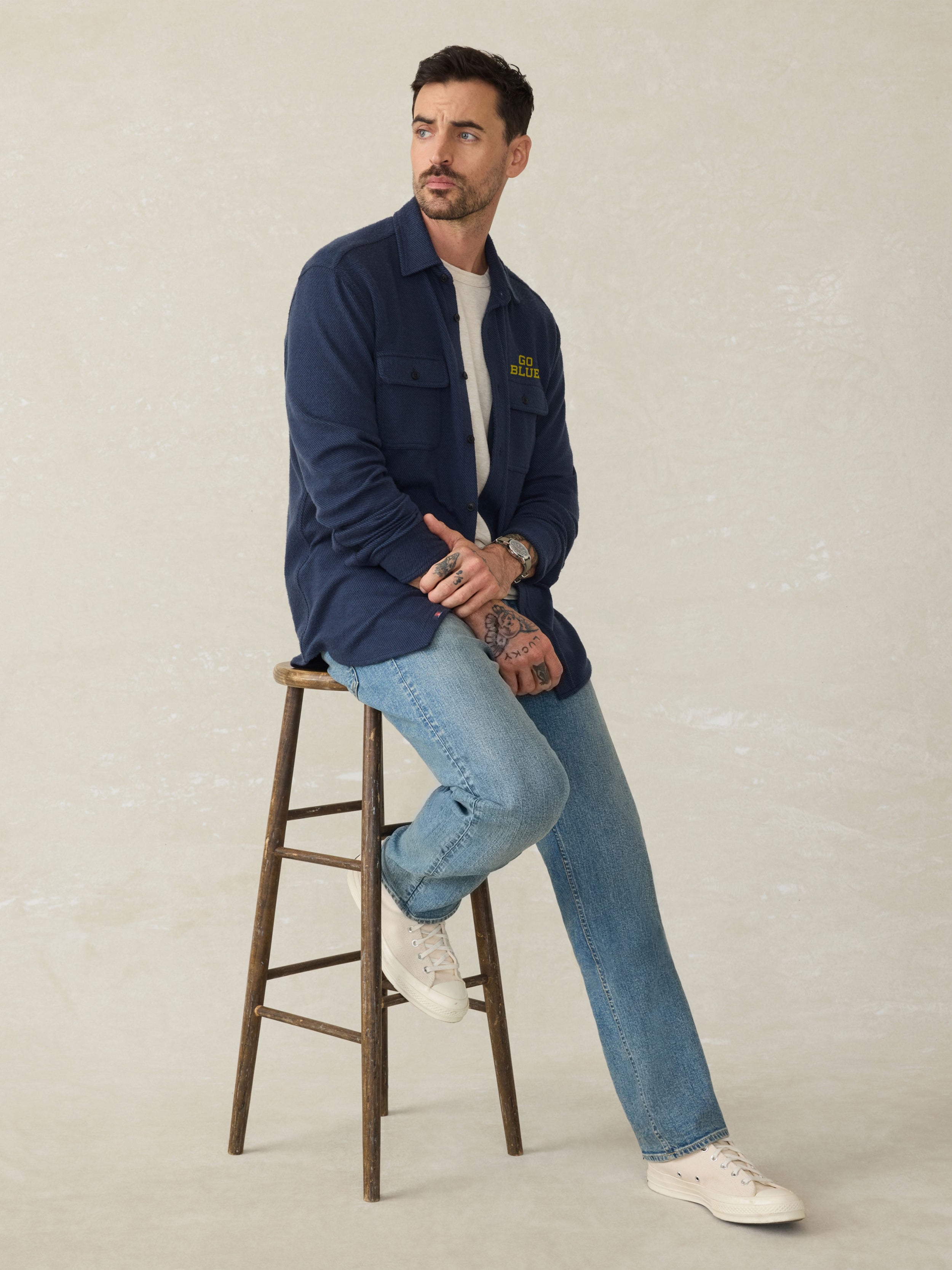 Man wearing a navy long sleeve button up shirt with Michigan graphic on left chest and left arm against a beige background