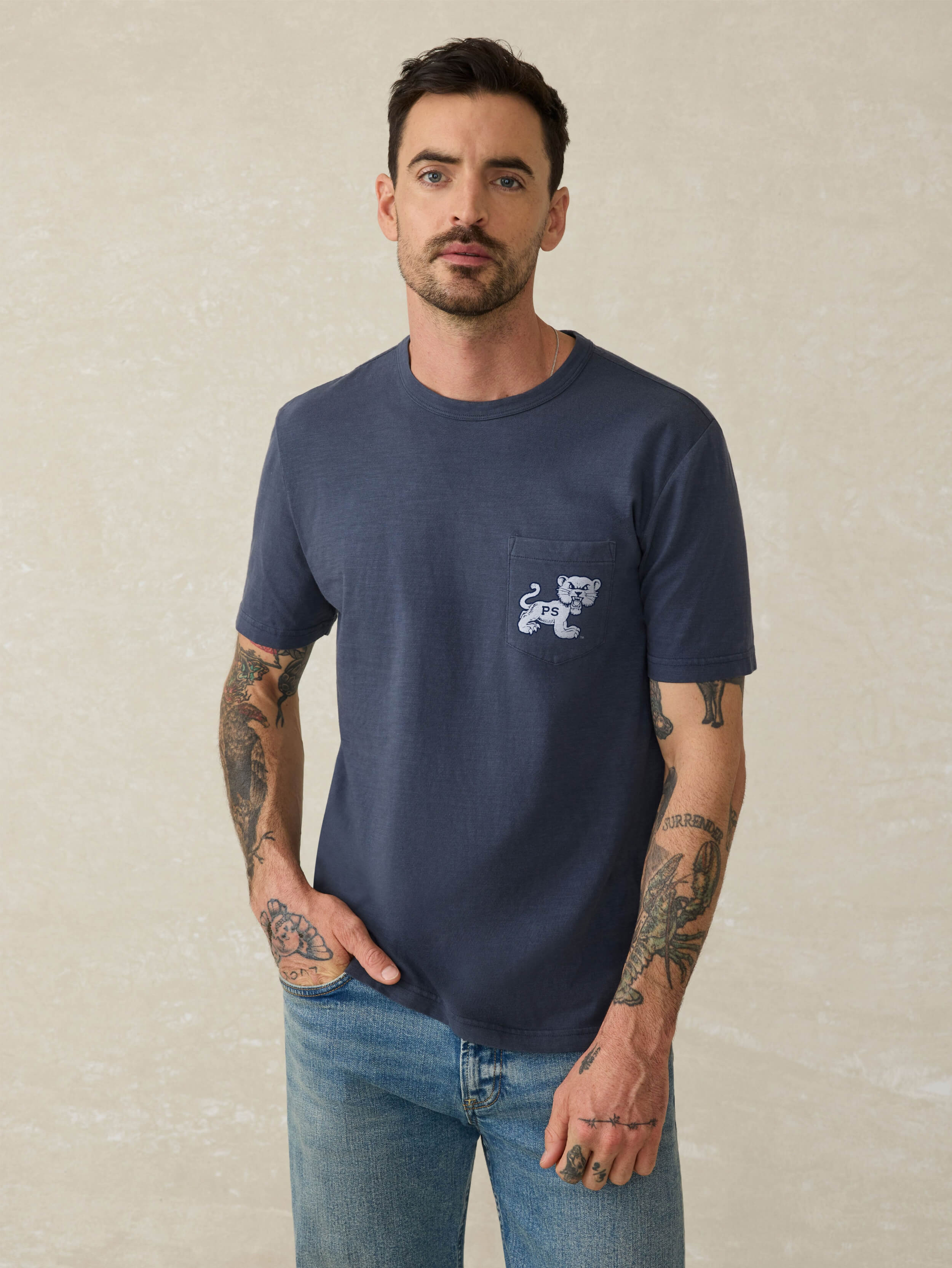 Man wearing a navy blue t-shirt with a Penn State graphic on the chest pocket against a beige background