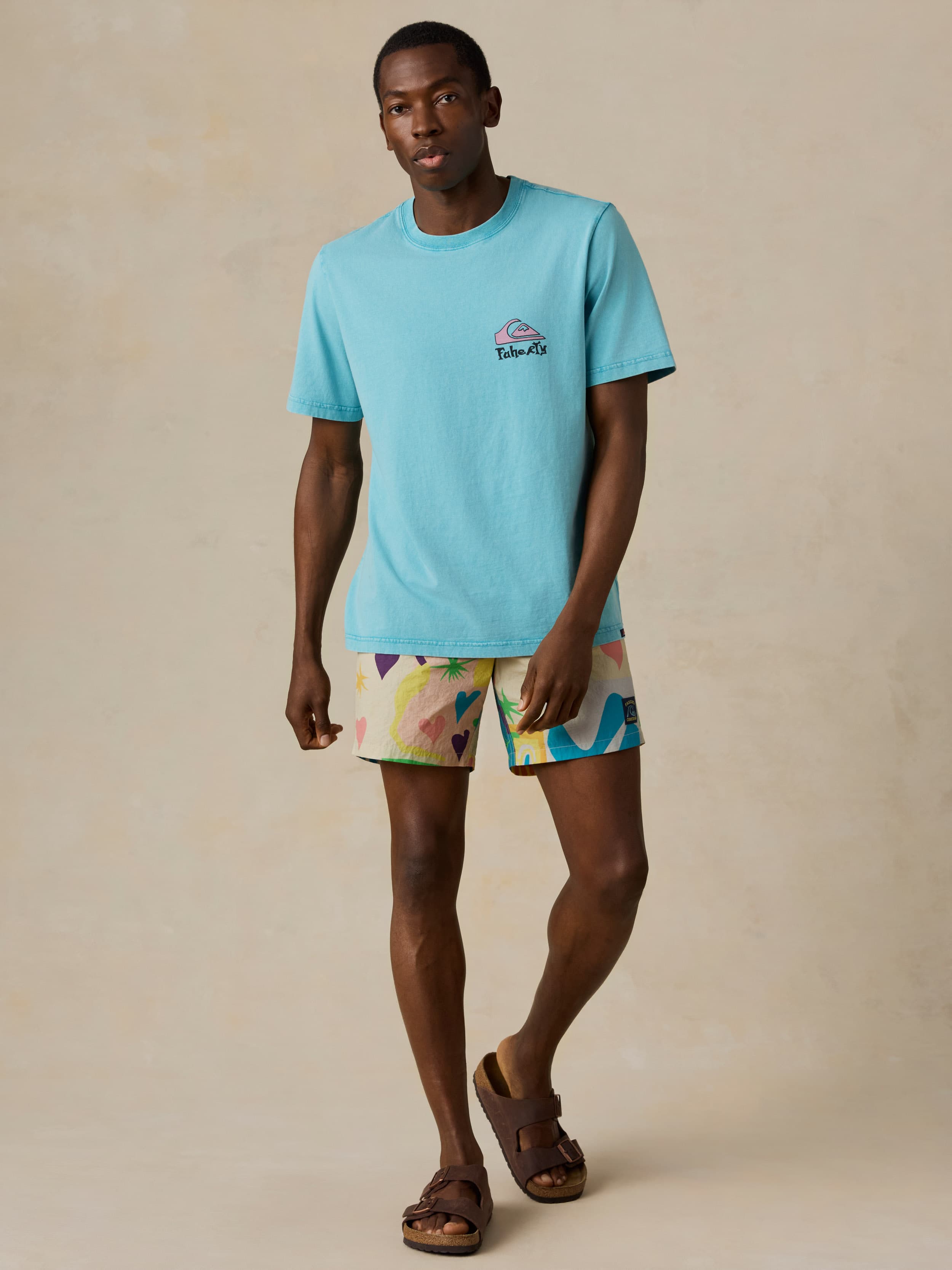 Man wearing a light blue t-shirt and colorful swim shorts on a beige background
