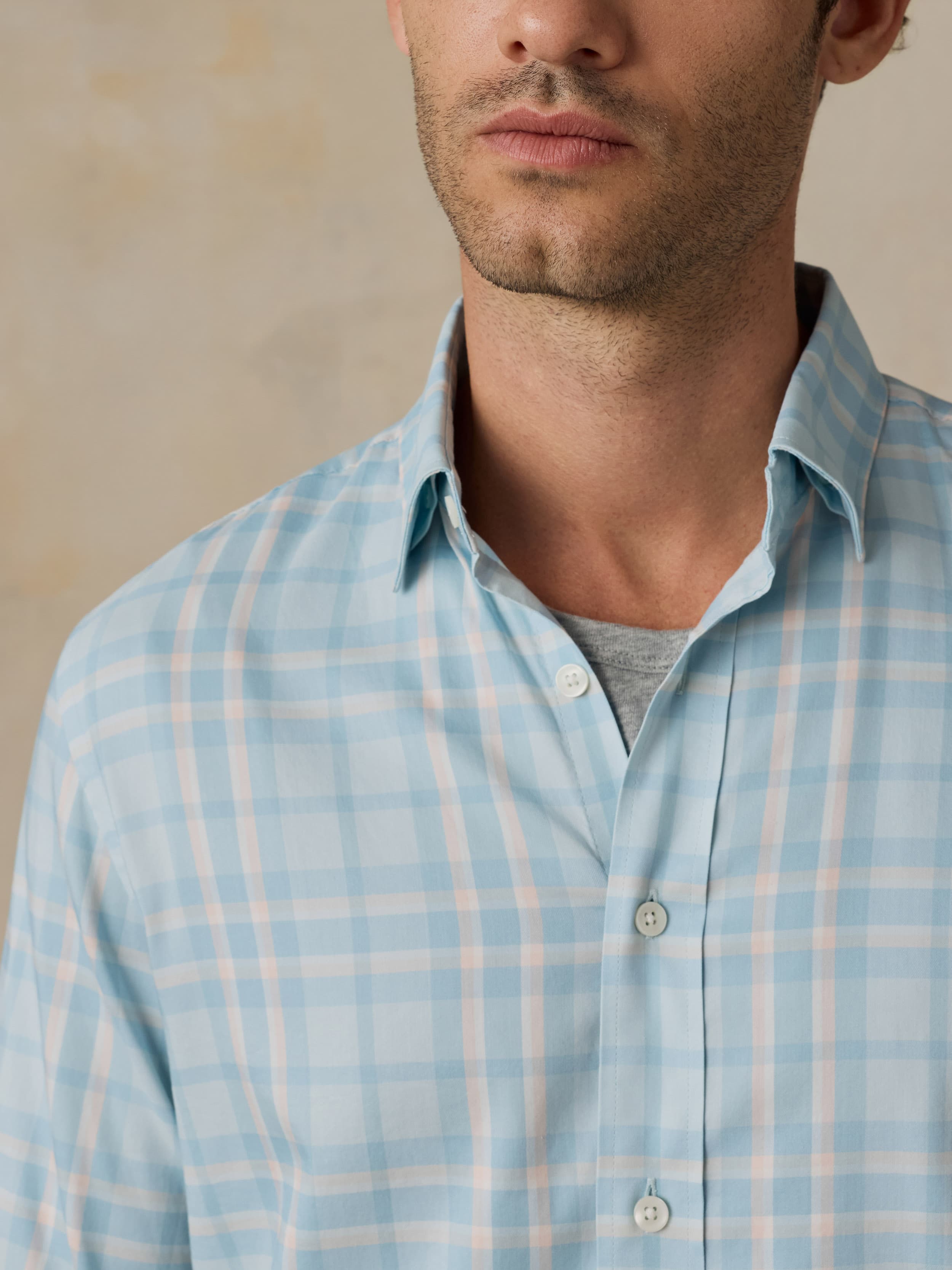 Close-up of a man wearing blue and white plaid shirt against a beige background