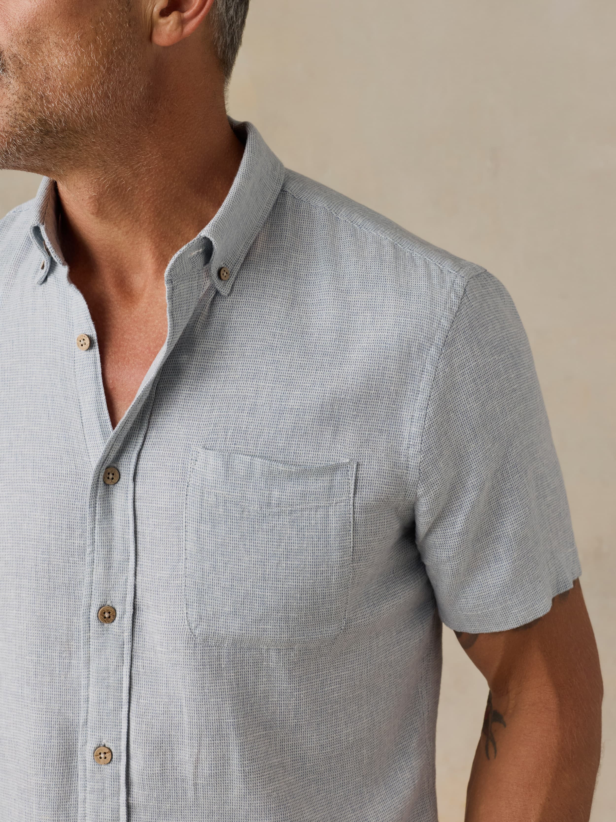 Man wearing a light blue short-sleeve shirt against a beige background