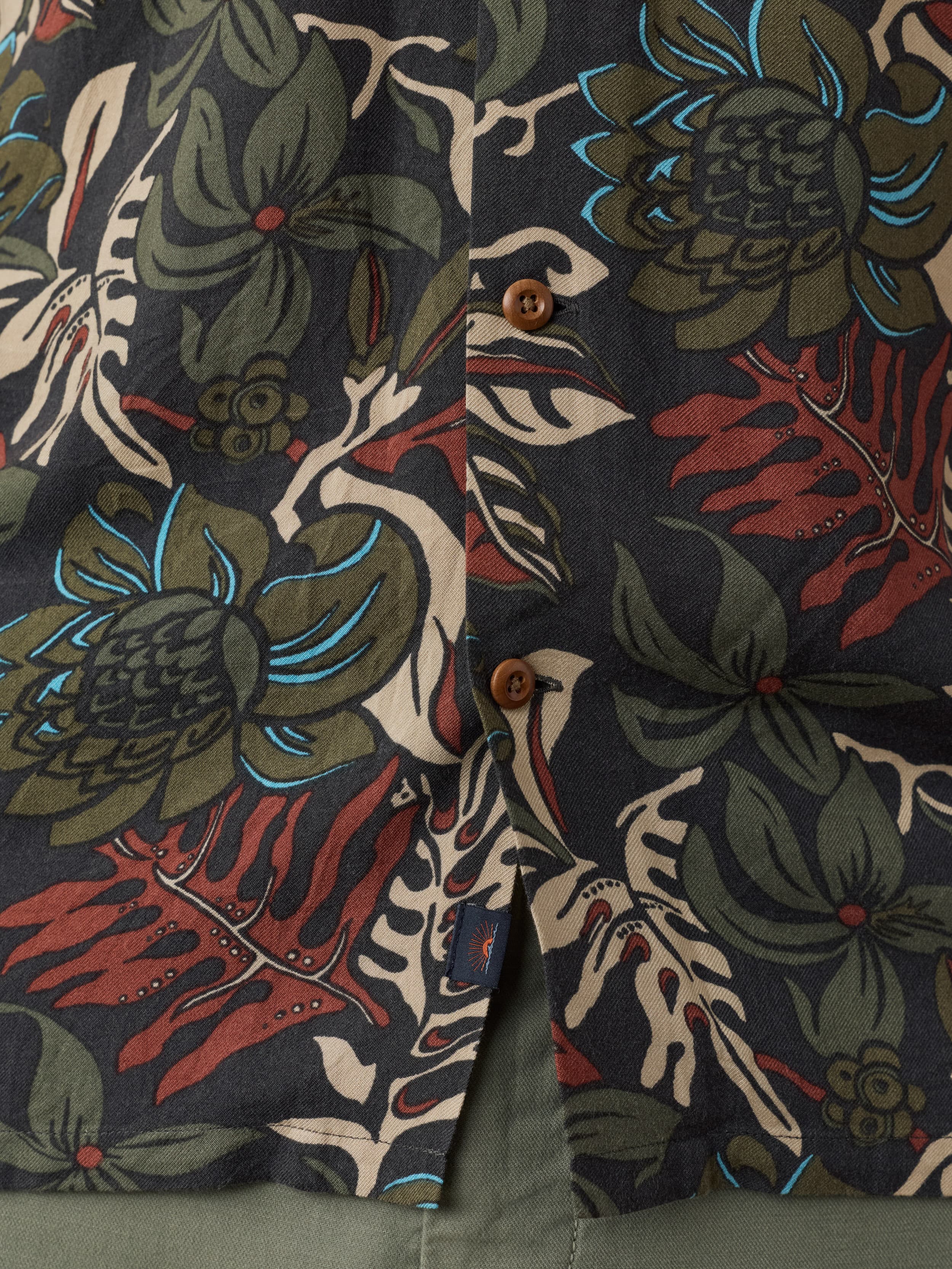 Close-up of a tropical patterned shirt with green, red, and brown colors.