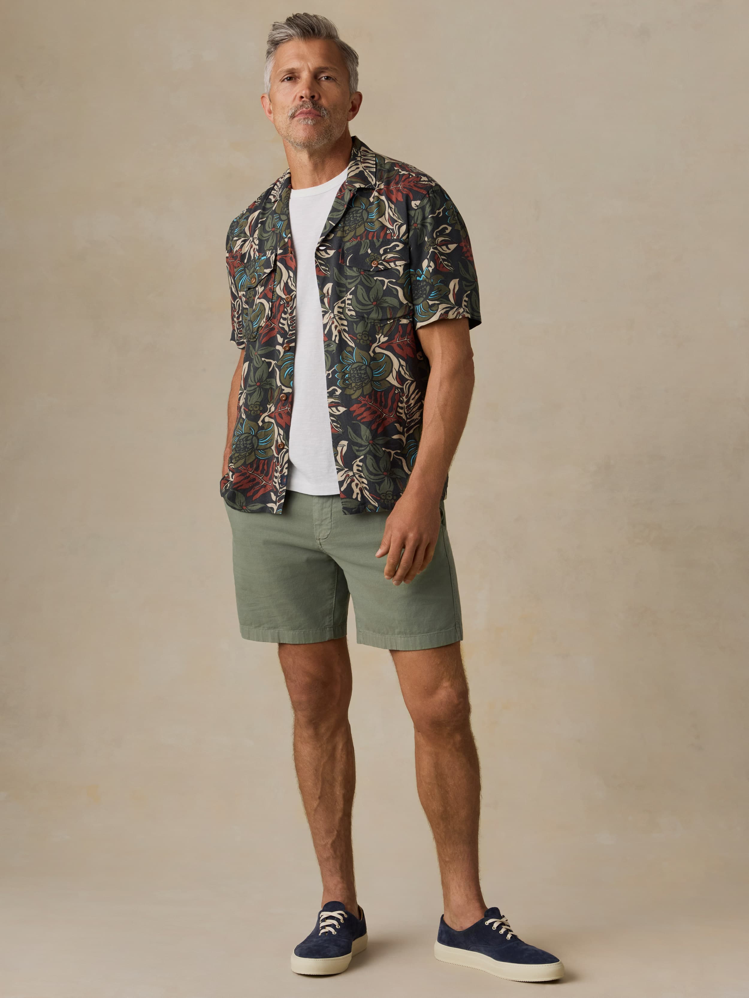 Man wearing a tropical patterned shirt and green shorts against a beige background