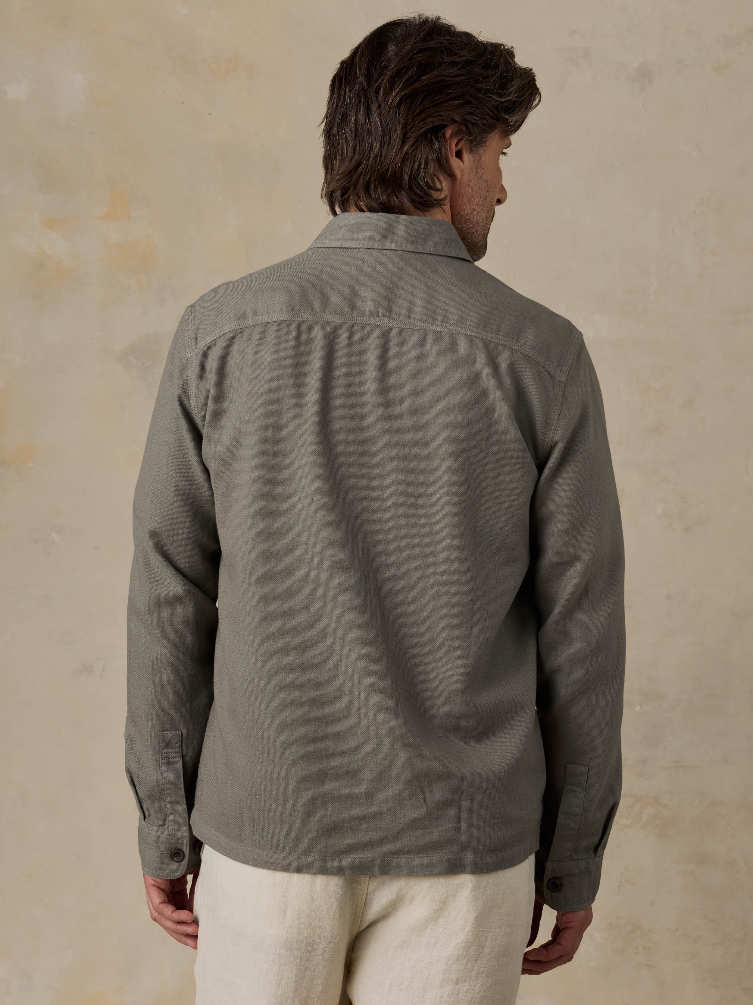 Man wearing an olive green jacket with beige pants against a beige background