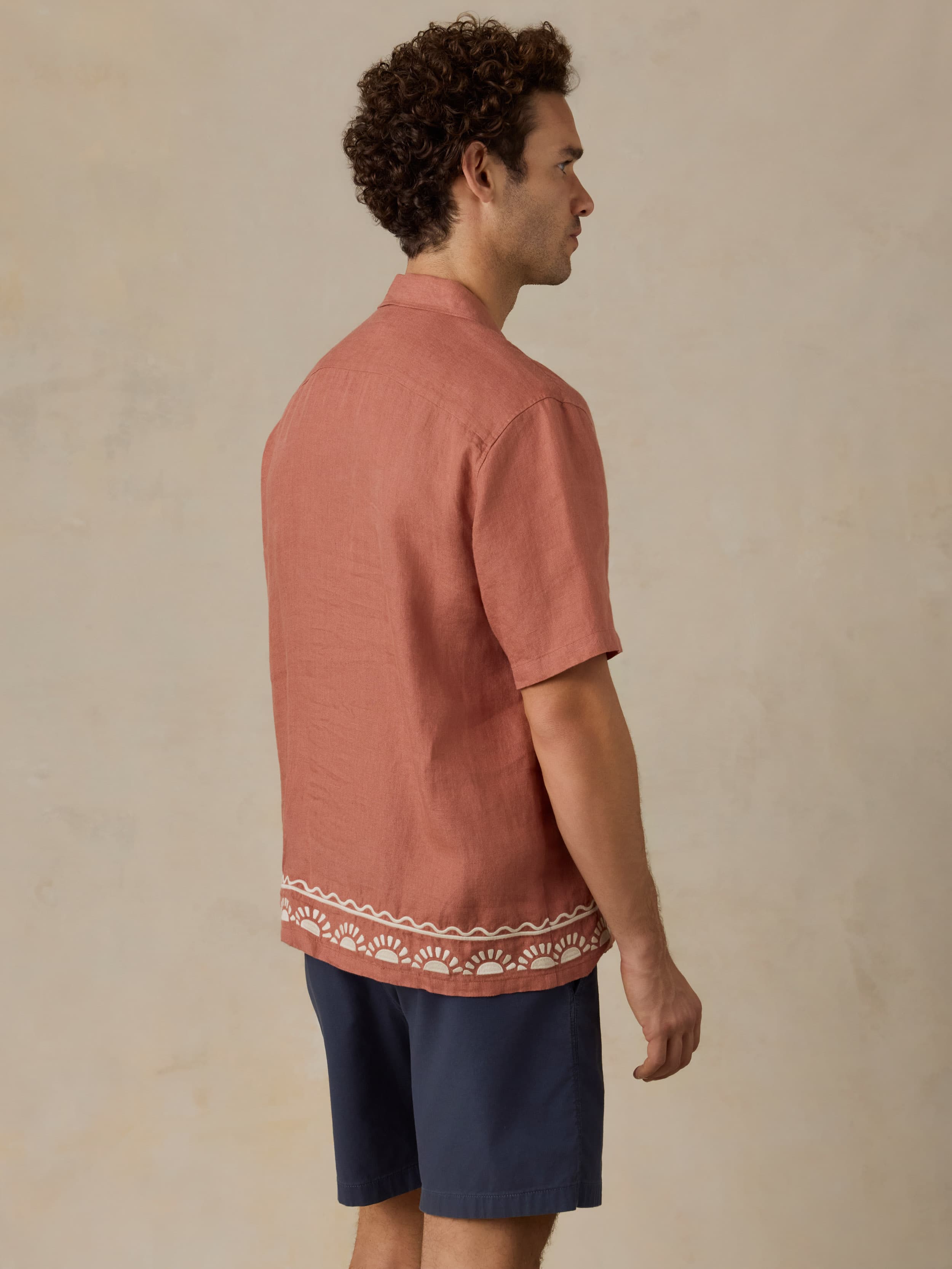 Man wearing a red patterned embroidered shirt and navy shorts against a beige background