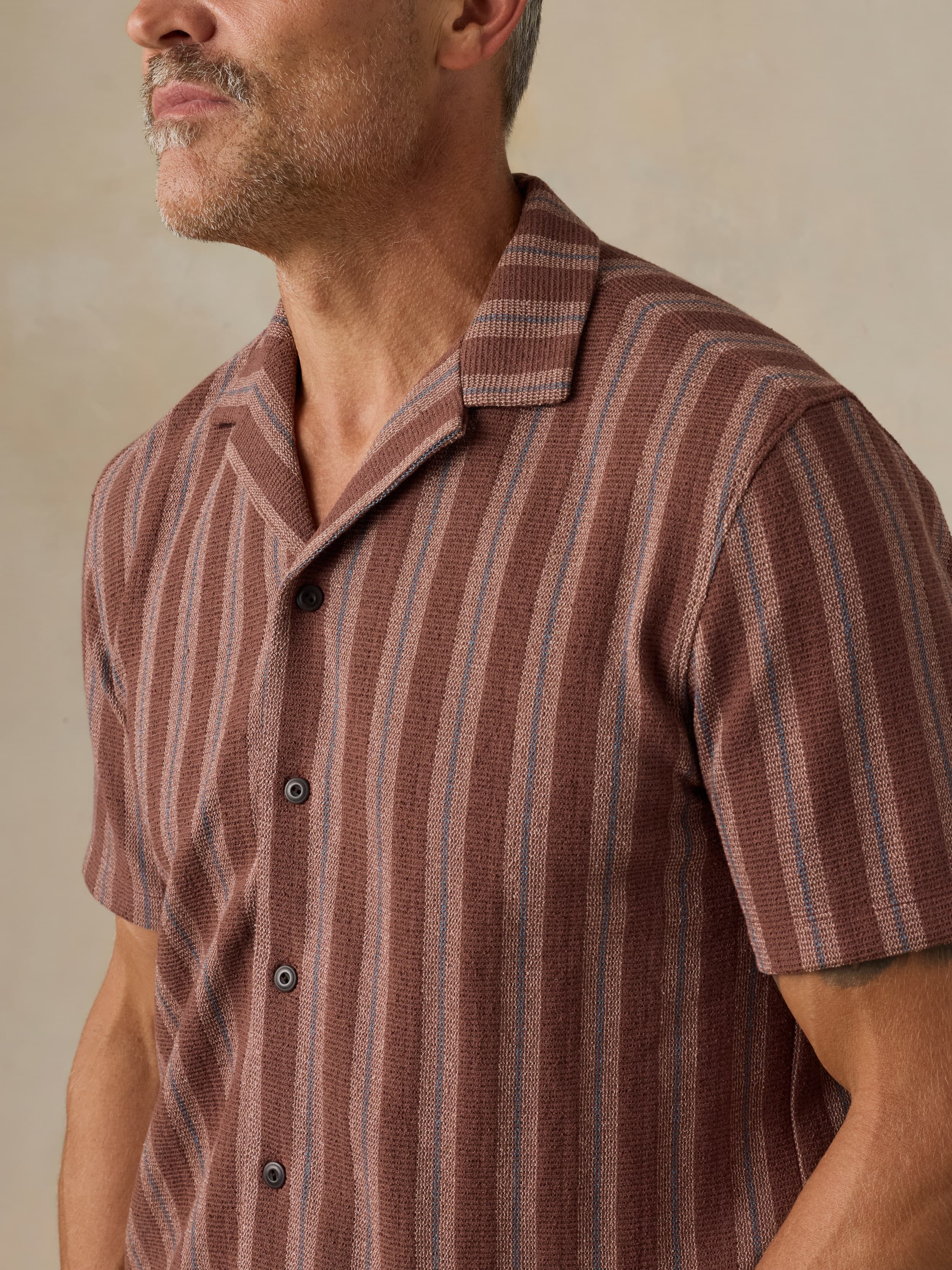 Man wearing a brown and red striped shirt against a beige background