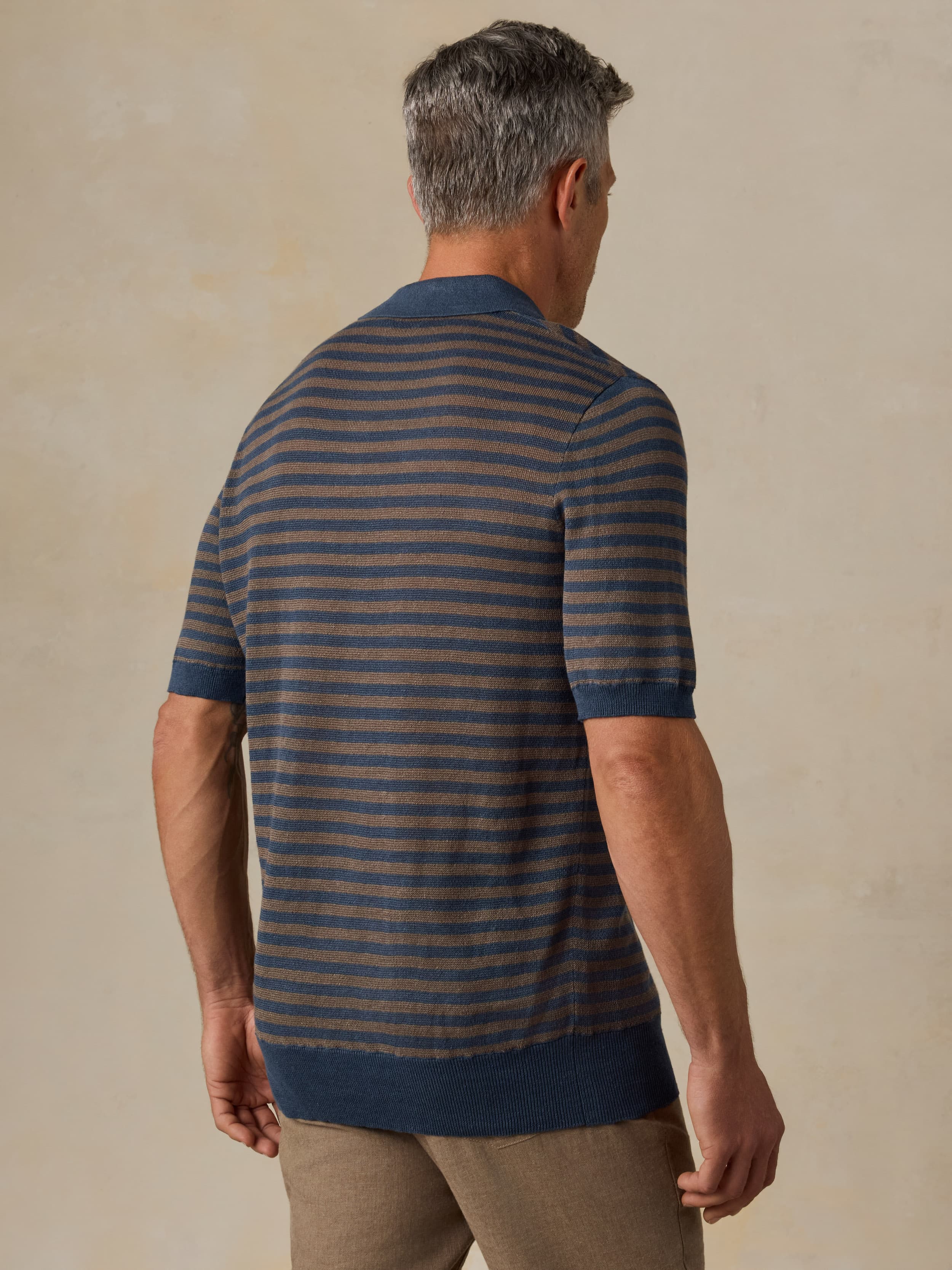 Man wearing a striped sweater polo against a beige background