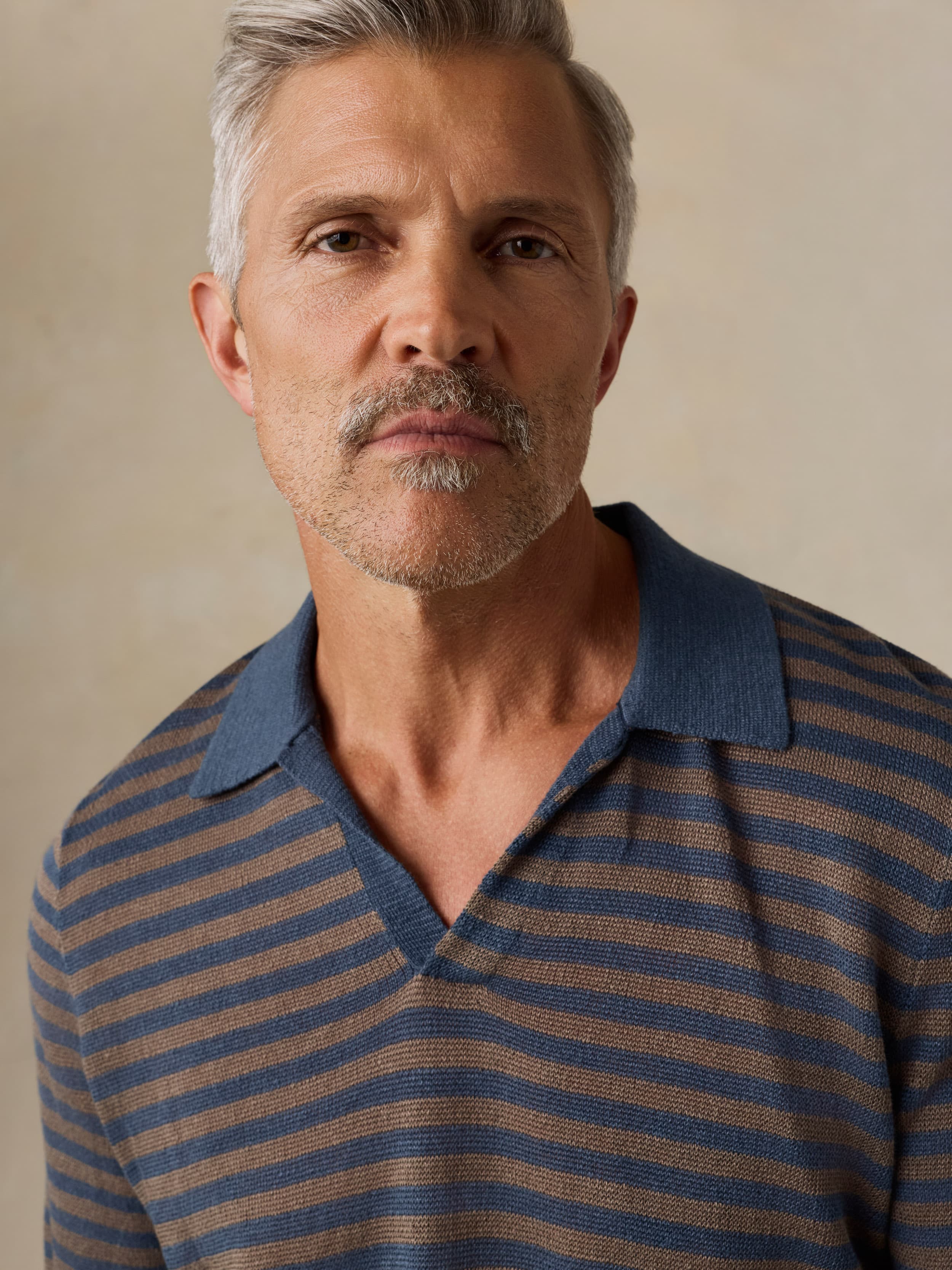 Man wearing a blue and brown striped shirt against a beige background