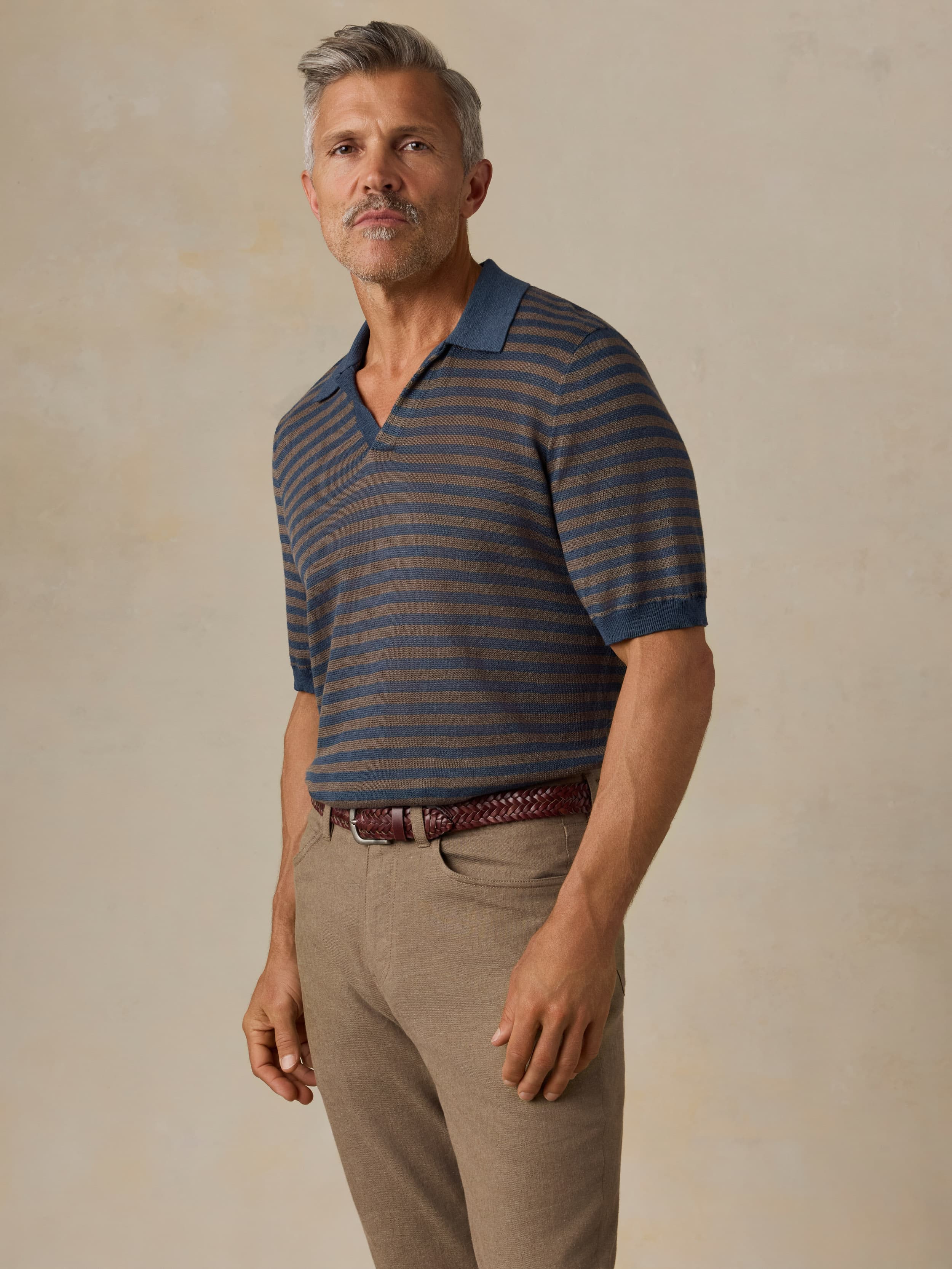Man wearing a striped polo shirt and beige pants against a beige background