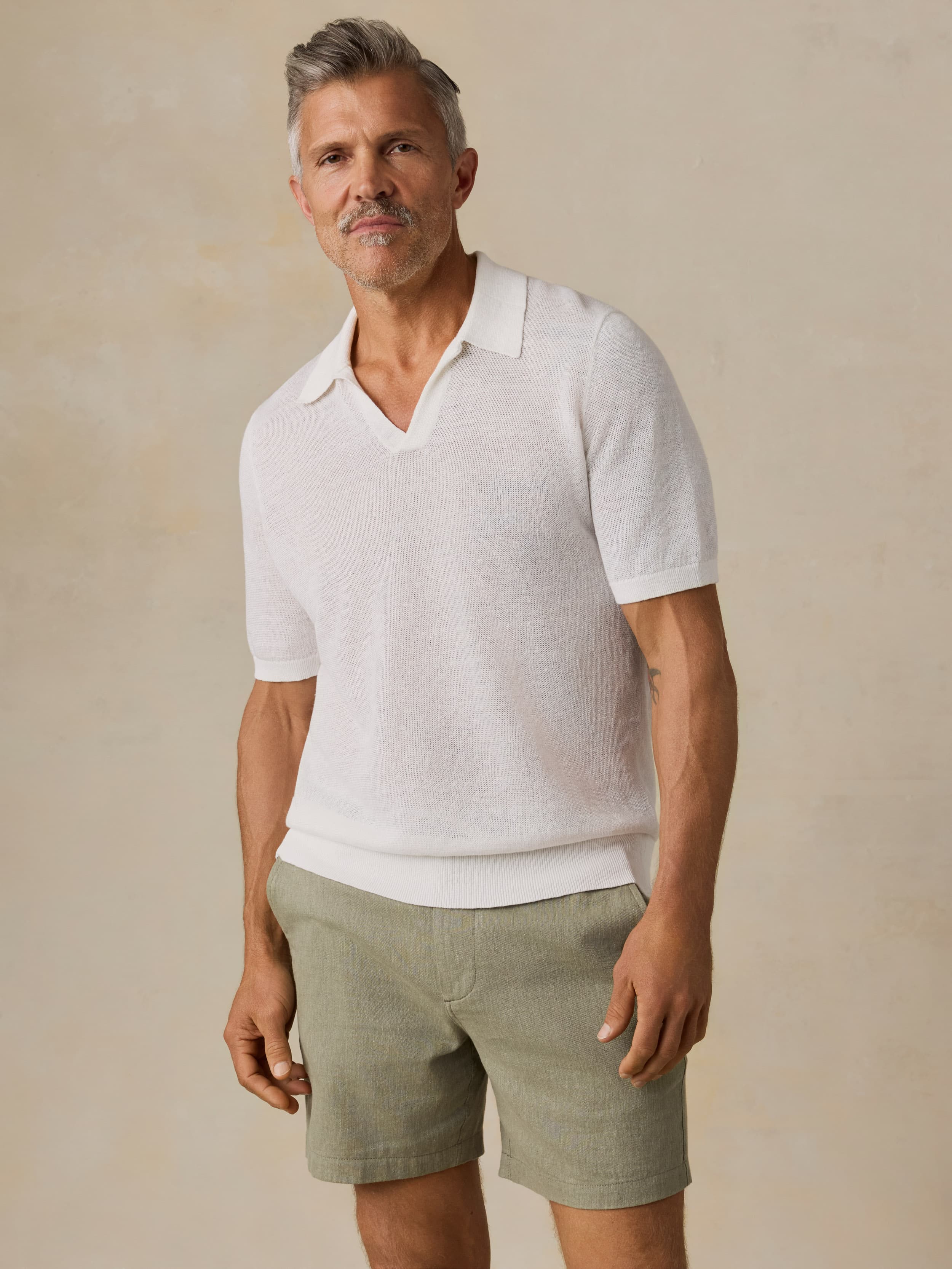 Man wearing a white polo shirt and green shorts against a beige background