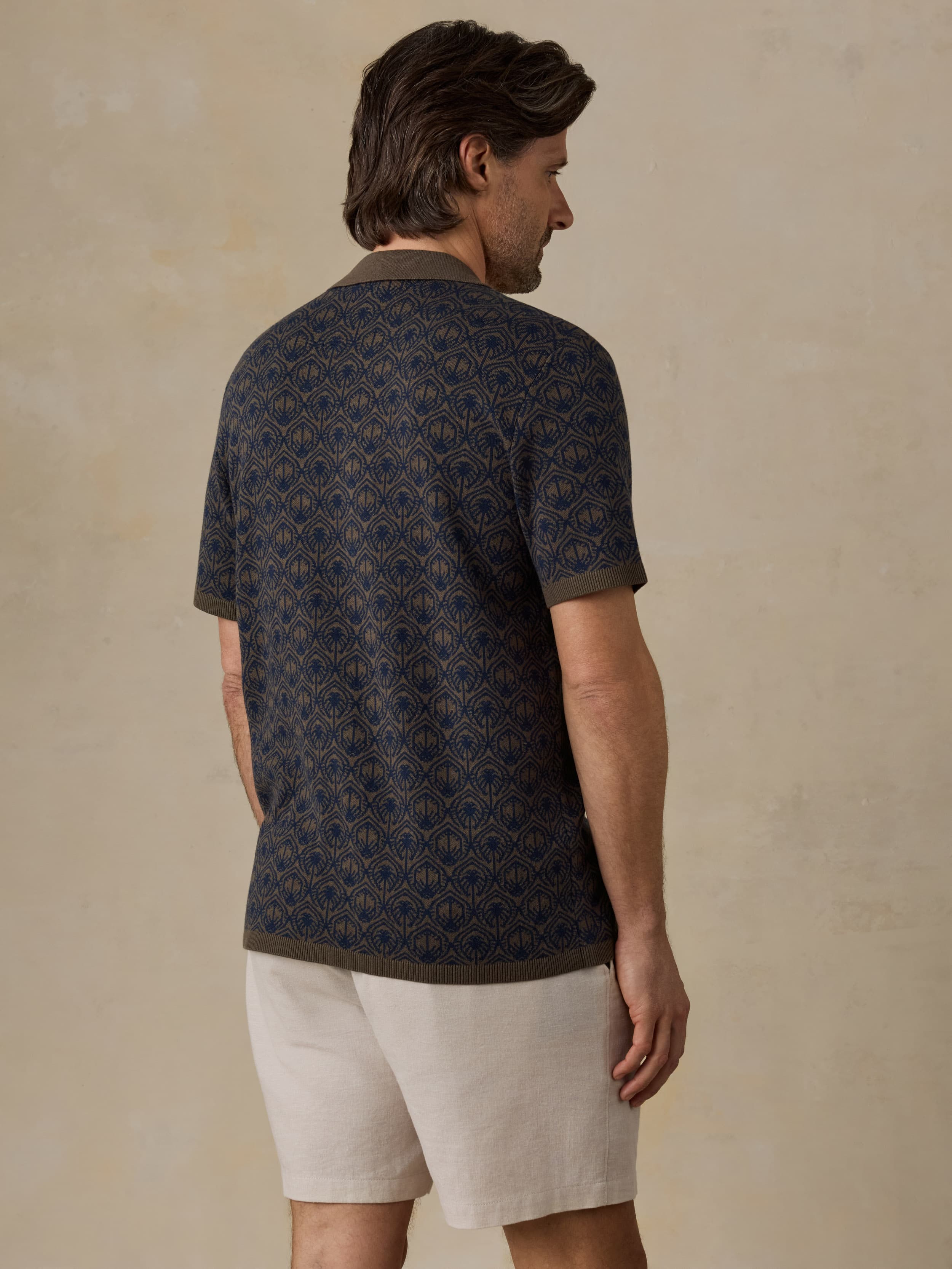Man wearing a patterned dark shirt and light shorts against a beige background