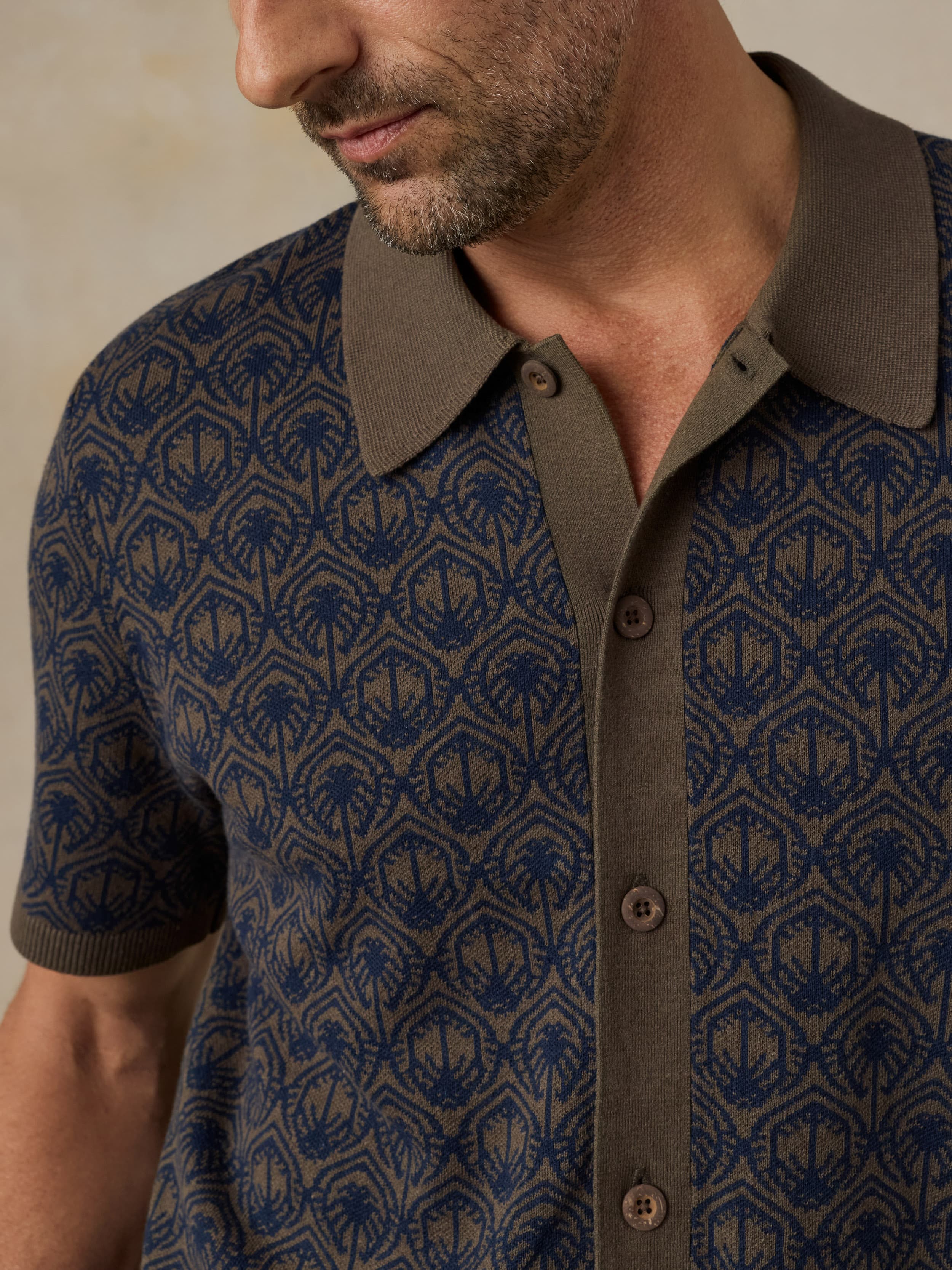 Man wearing a patterned shirt with a brown collar and buttons.