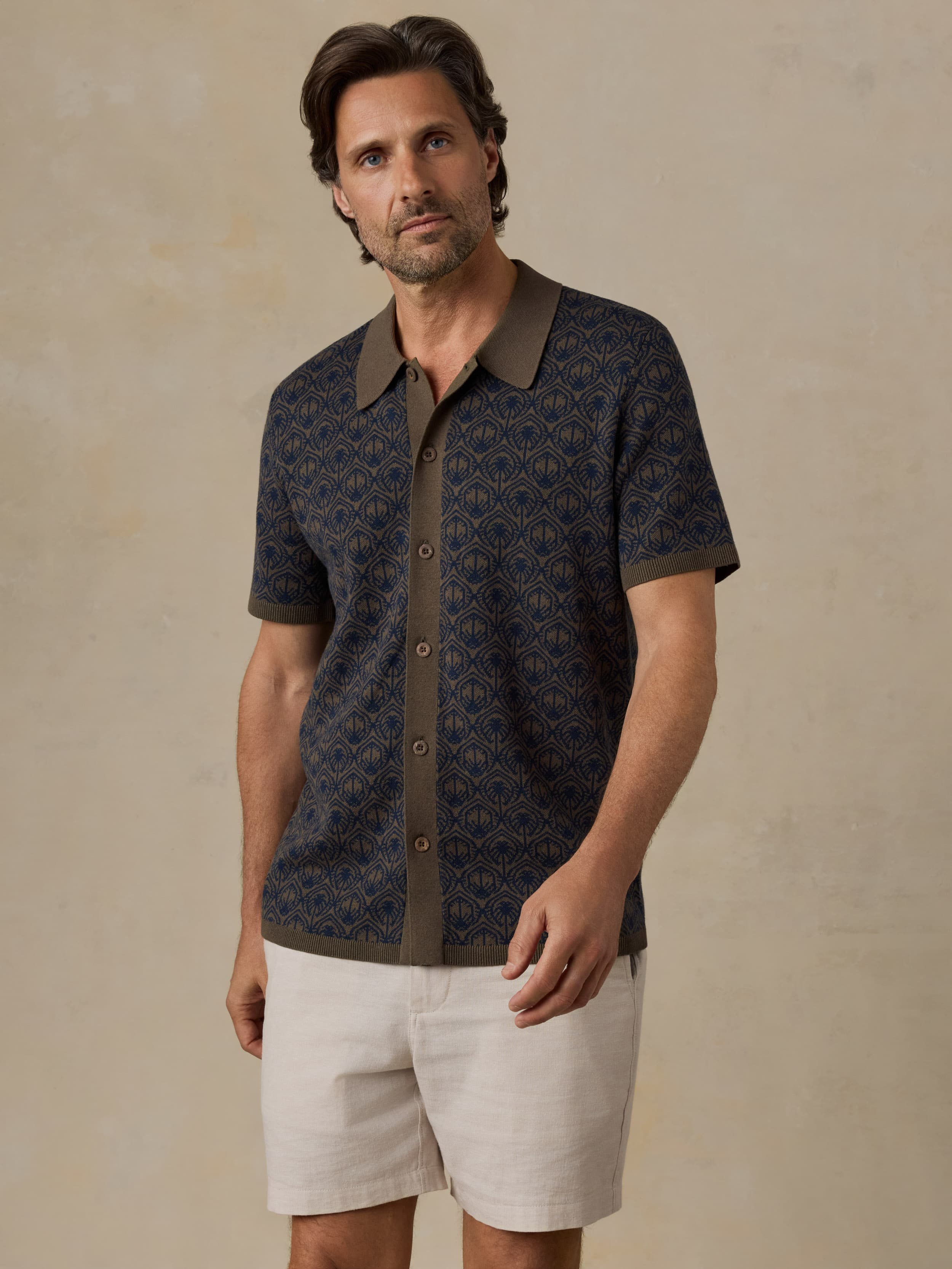 Man wearing a patterned shirt with a collar and white shorts on a beige background