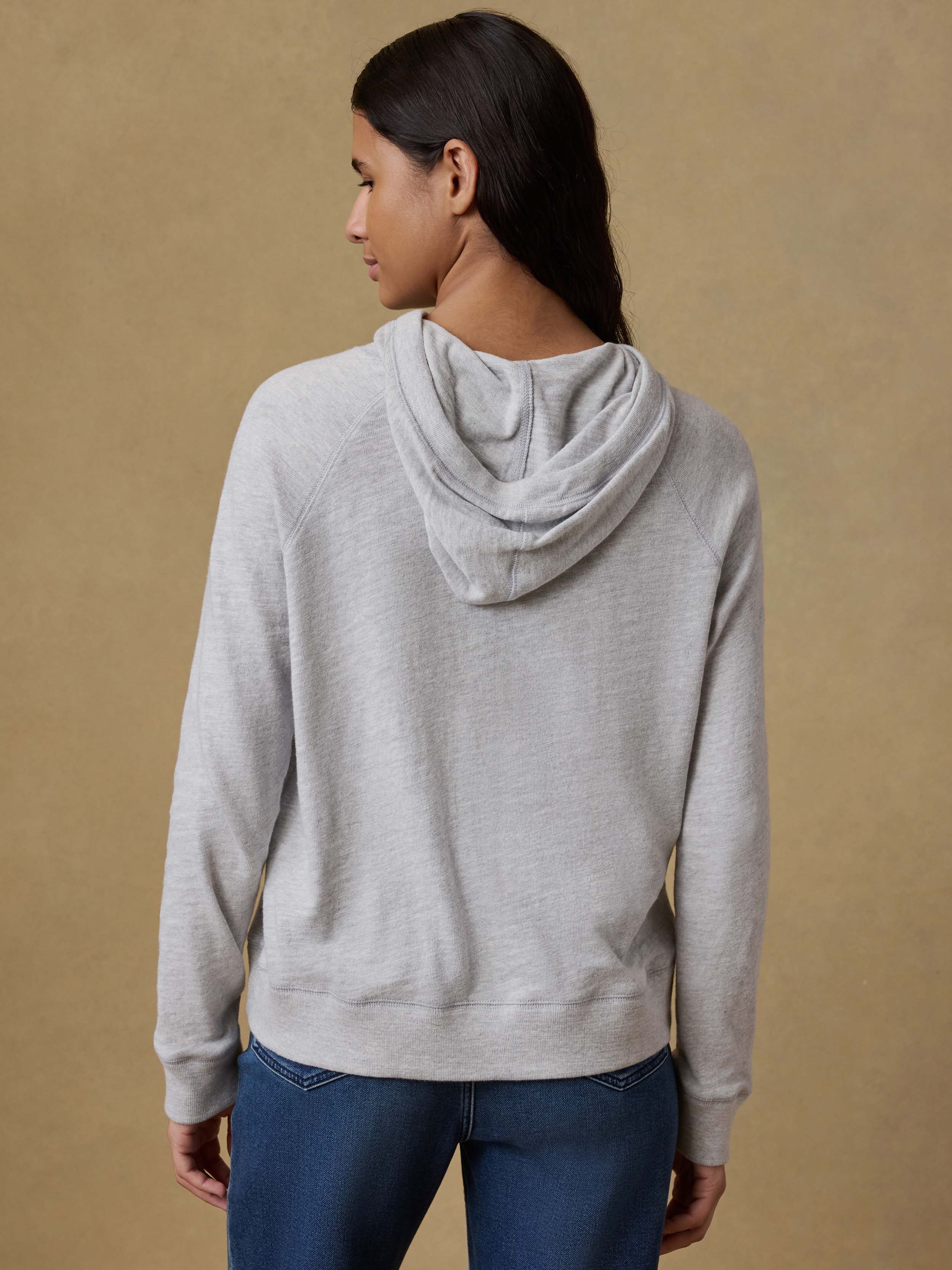 Woman wearing a gray hoodie and blue jeans against a beige background
