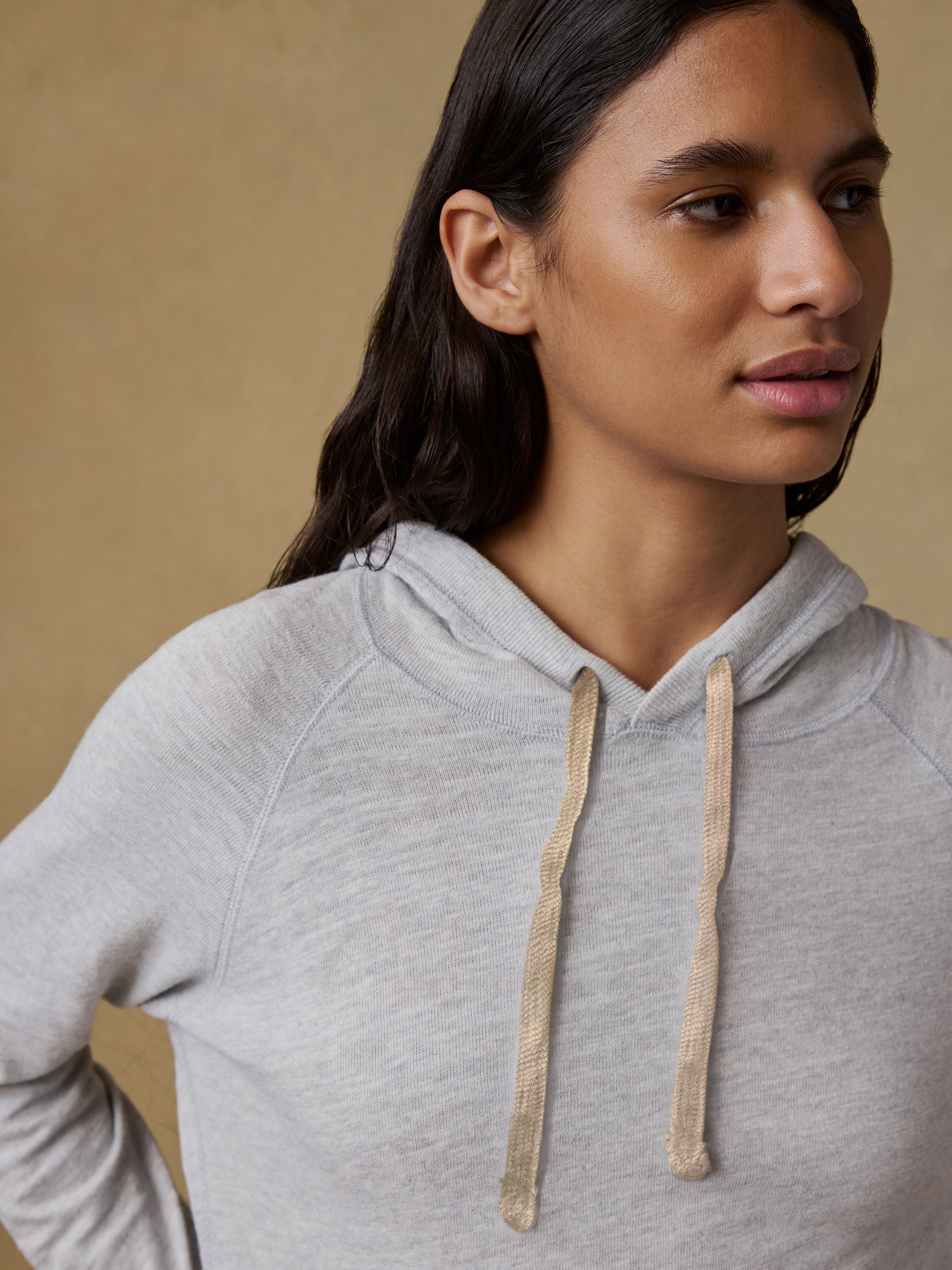 Woman wearing a gray hoodie and blue jeans against a beige background