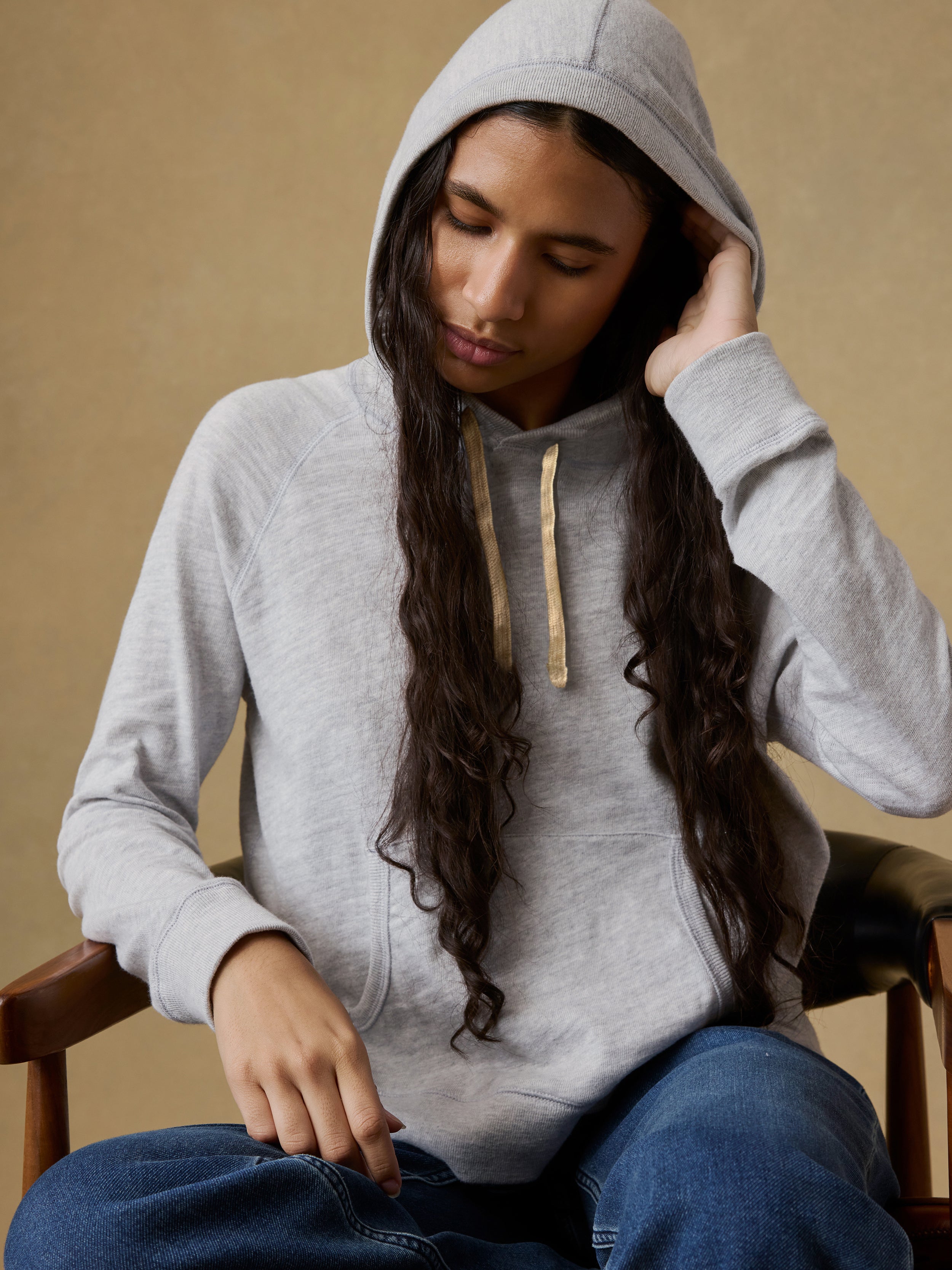 Woman wearing a gray hoodie and blue jeans against a beige background