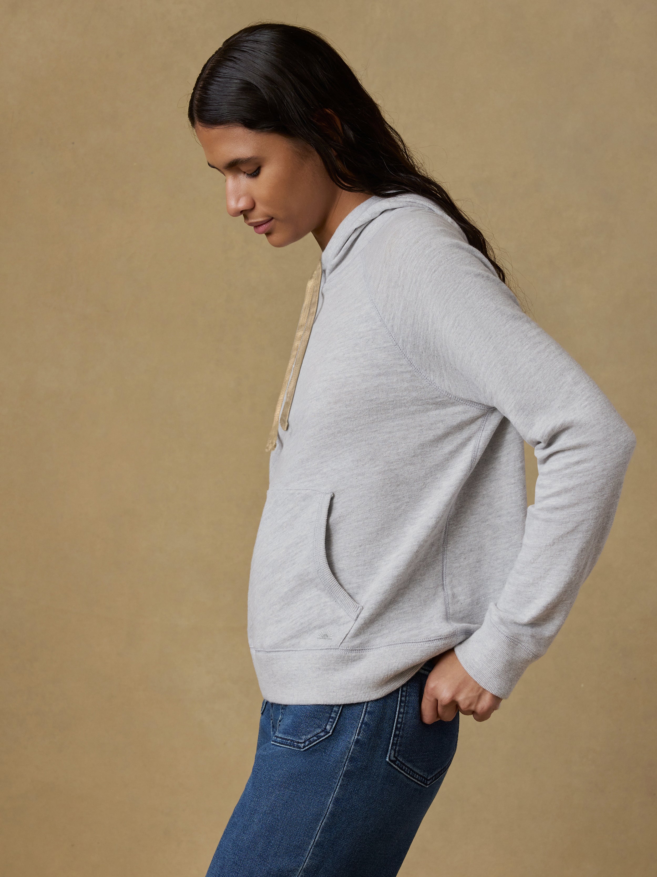 Woman wearing a gray hoodie and blue jeans against a beige background