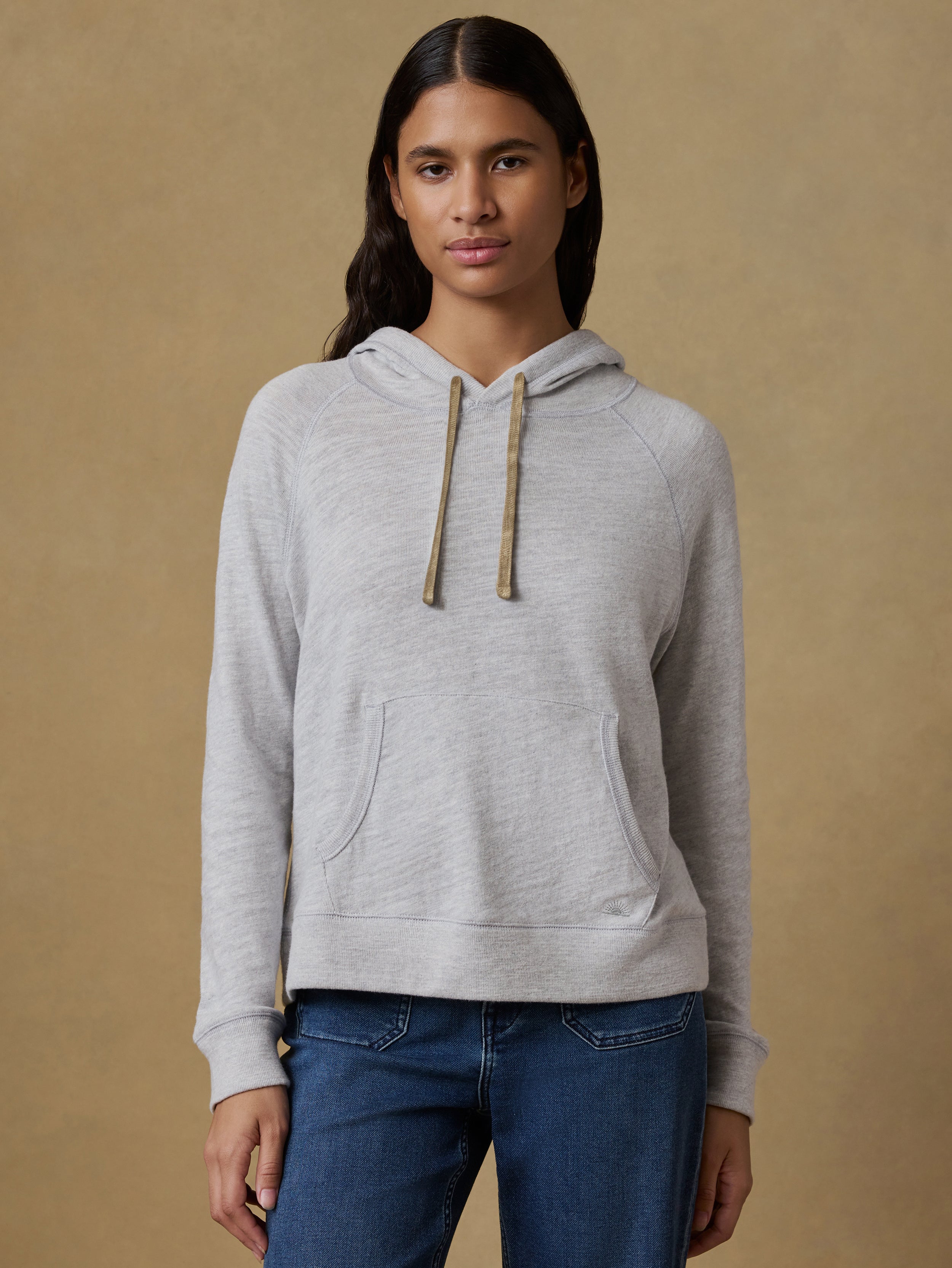 Woman wearing a gray hoodie and blue jeans against a beige background