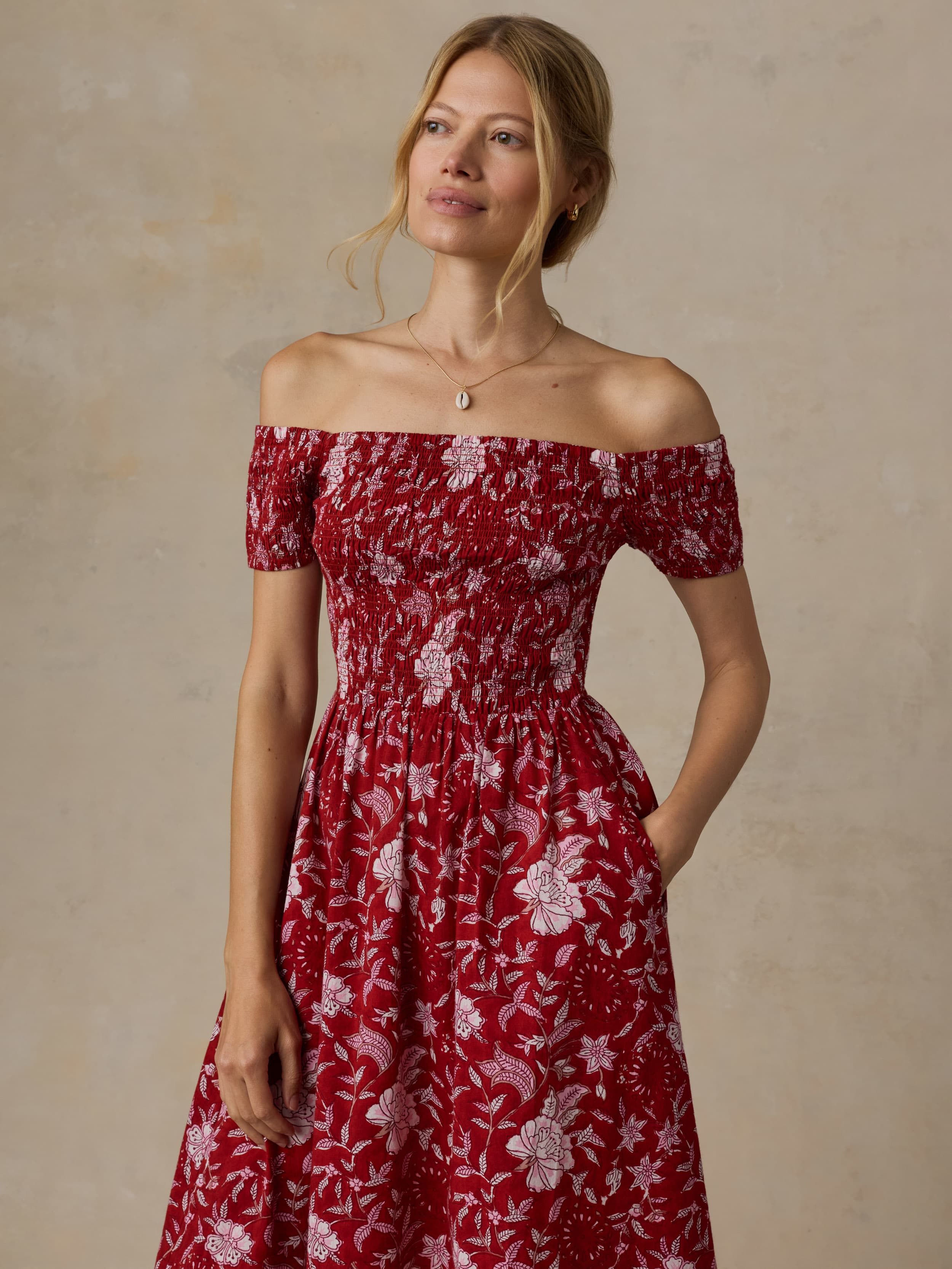 Woman wearing a red floral off-shoulder dress against a beige background