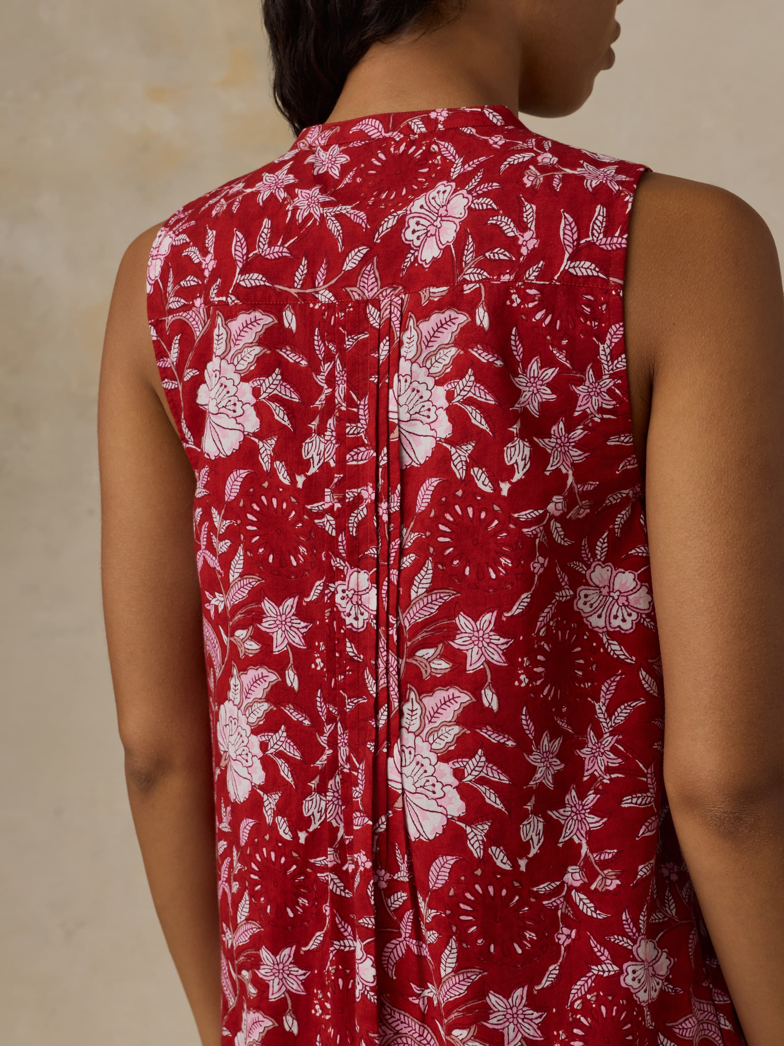 Red sleeveless dress with white floral pattern worn by a woman against a beige background