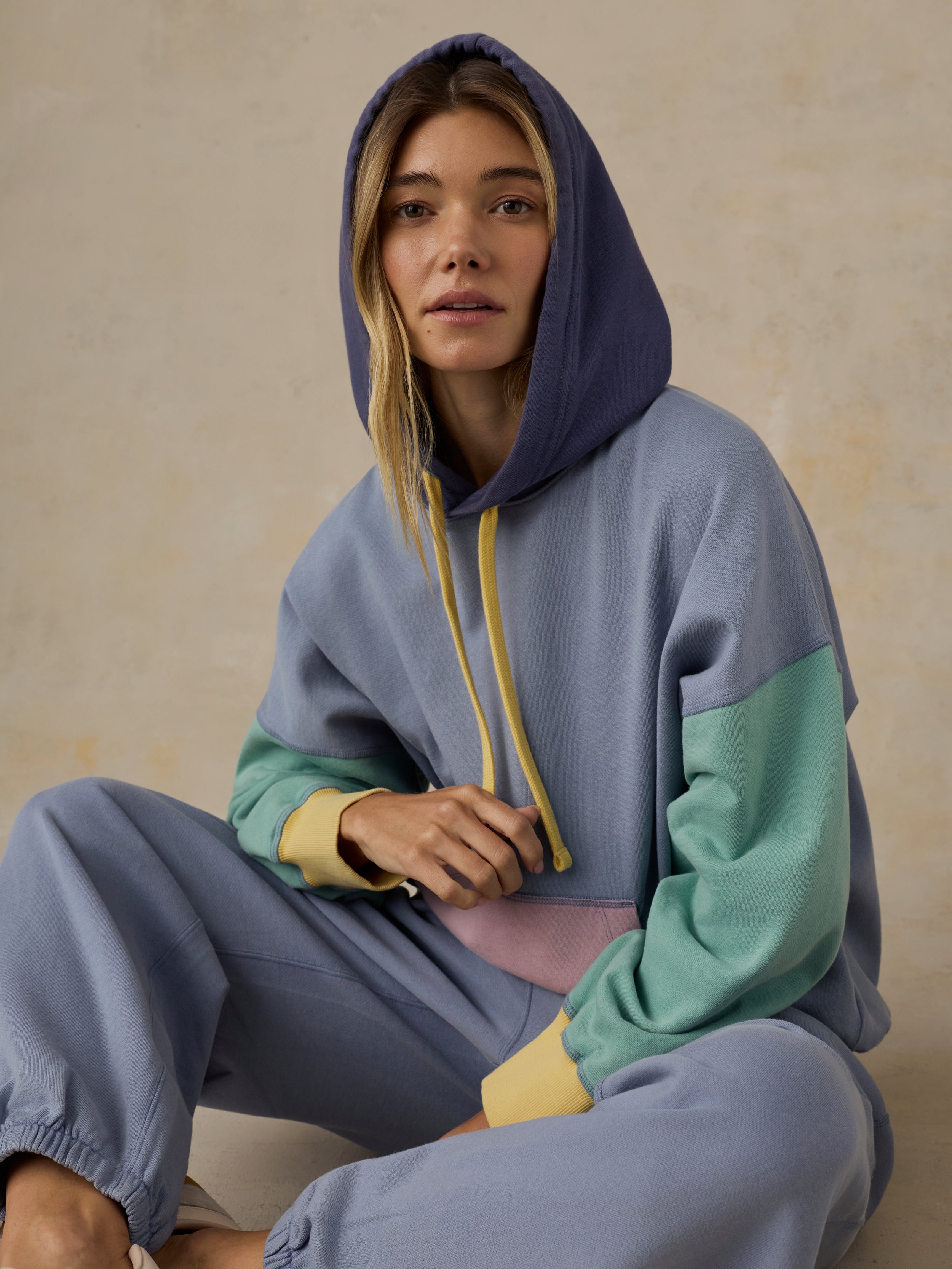 Woman wearing a colorful hoodie and sweatpants sitting on the floor.