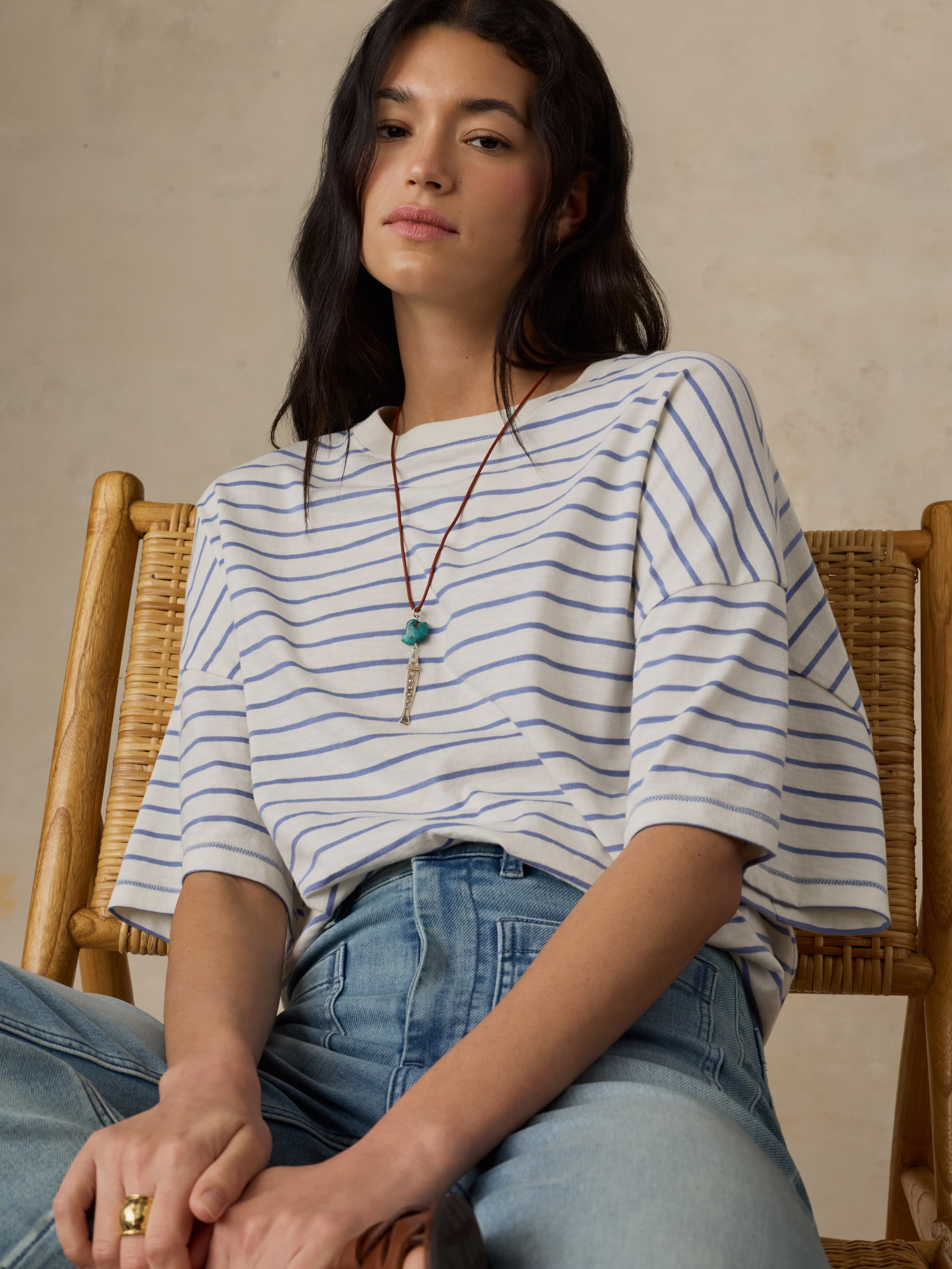 Woman wearing a striped shirt and jeans sitting on a wooden chair.