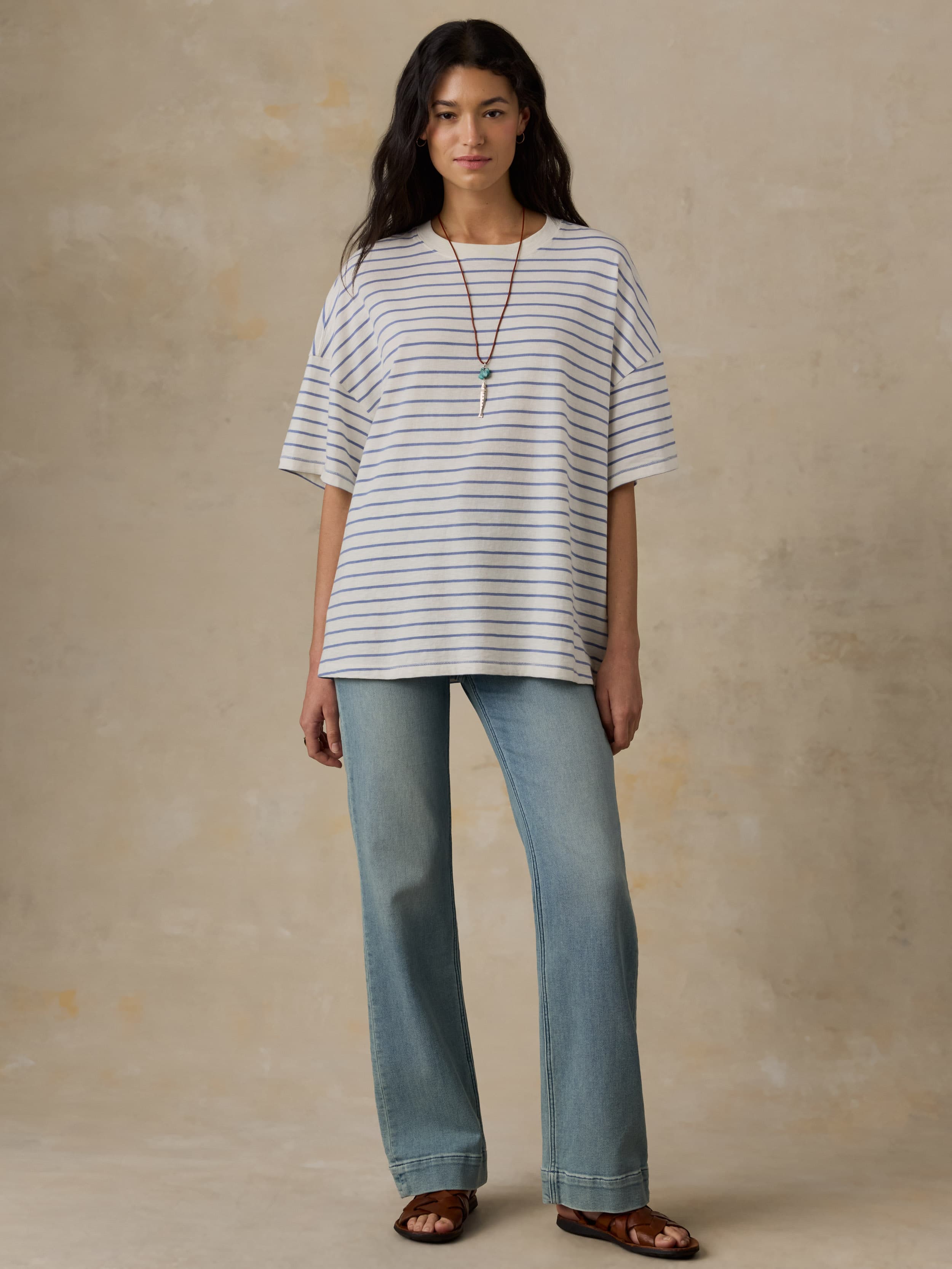 Woman wearing a striped shirt and light blue jeans against a beige background