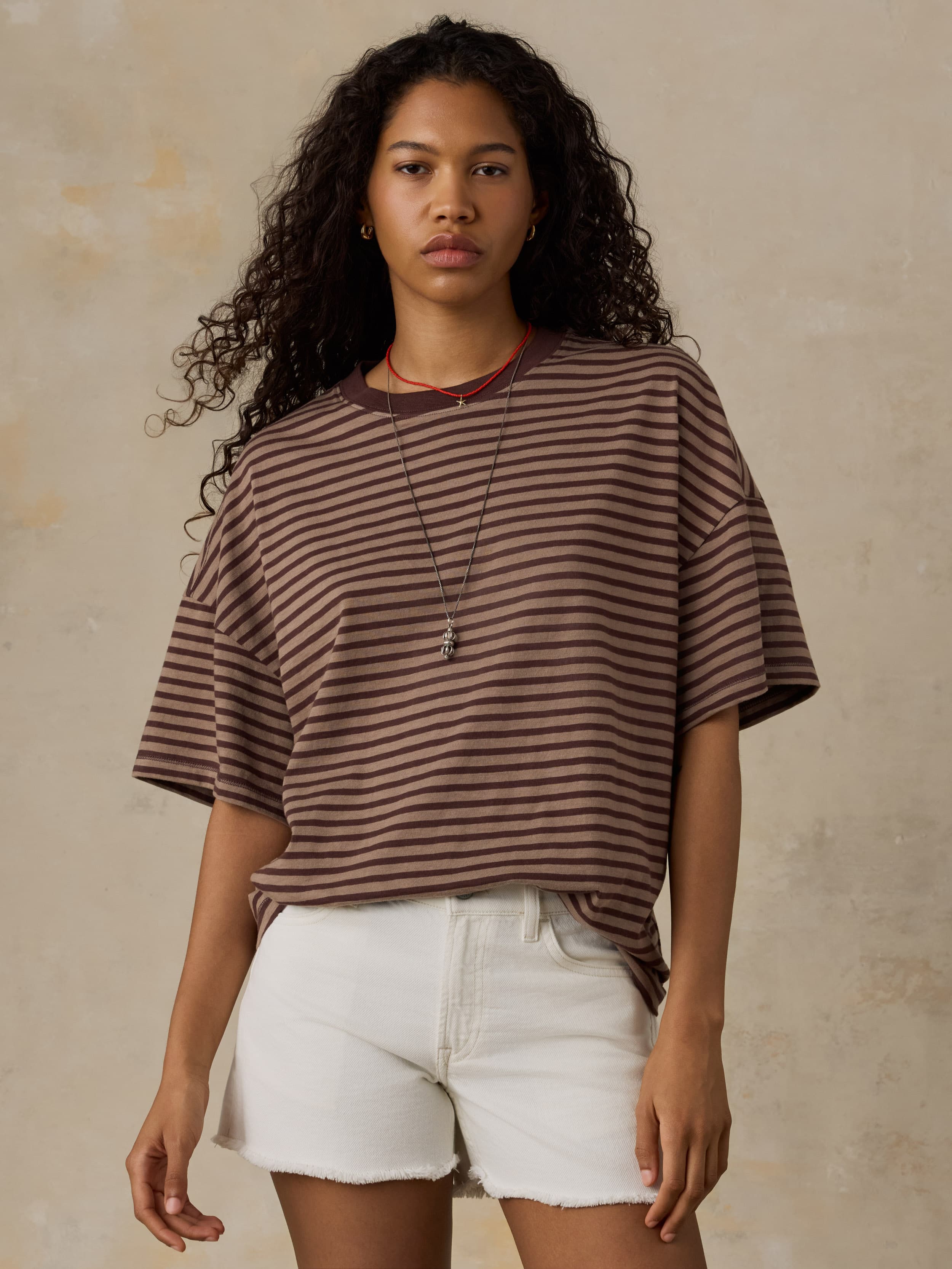 Woman wearing a brown striped shirt and white shorts against a beige background