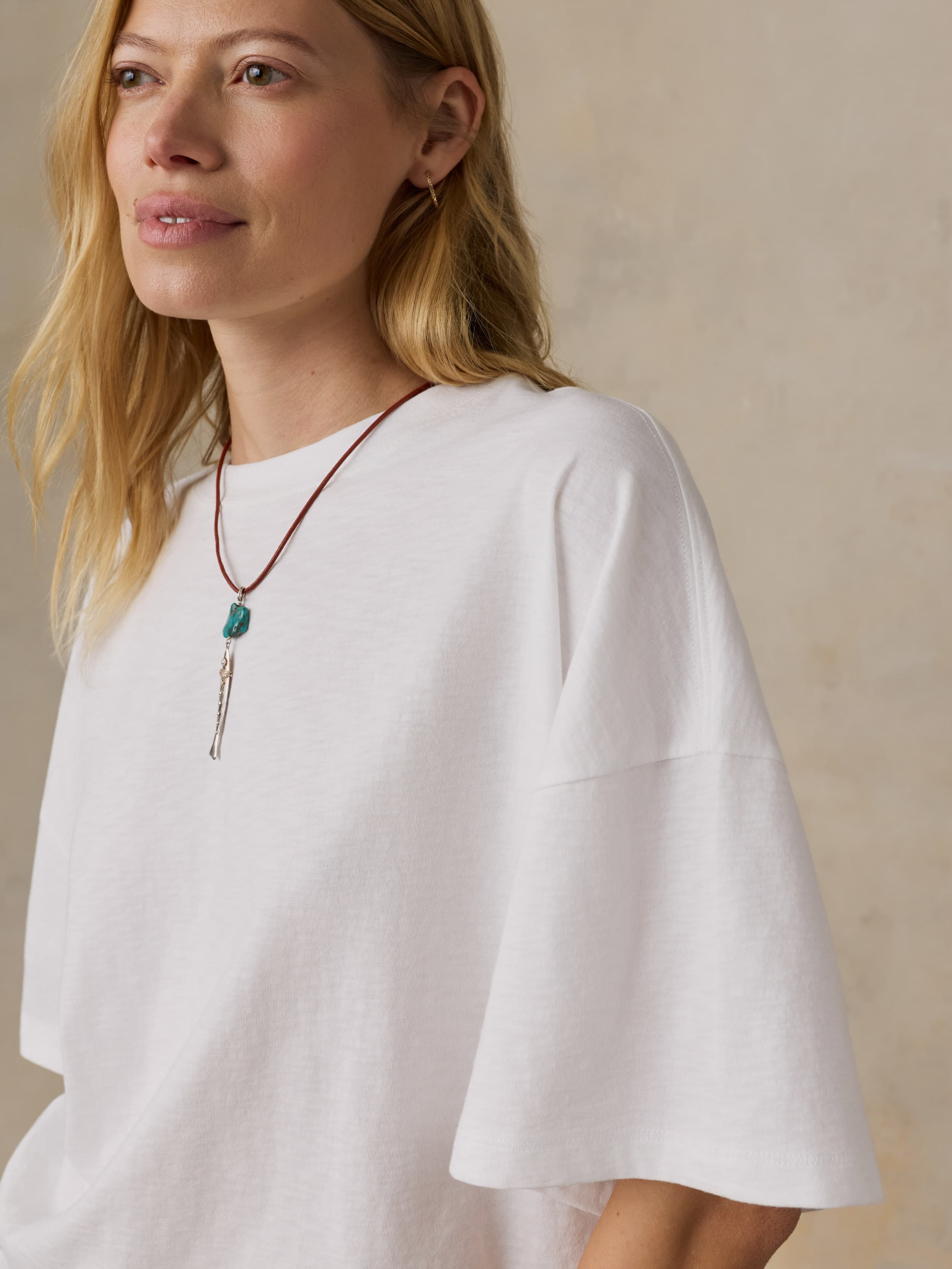 Woman wearing a white oversized t-shirt and a necklace with a pendant against a neutral background