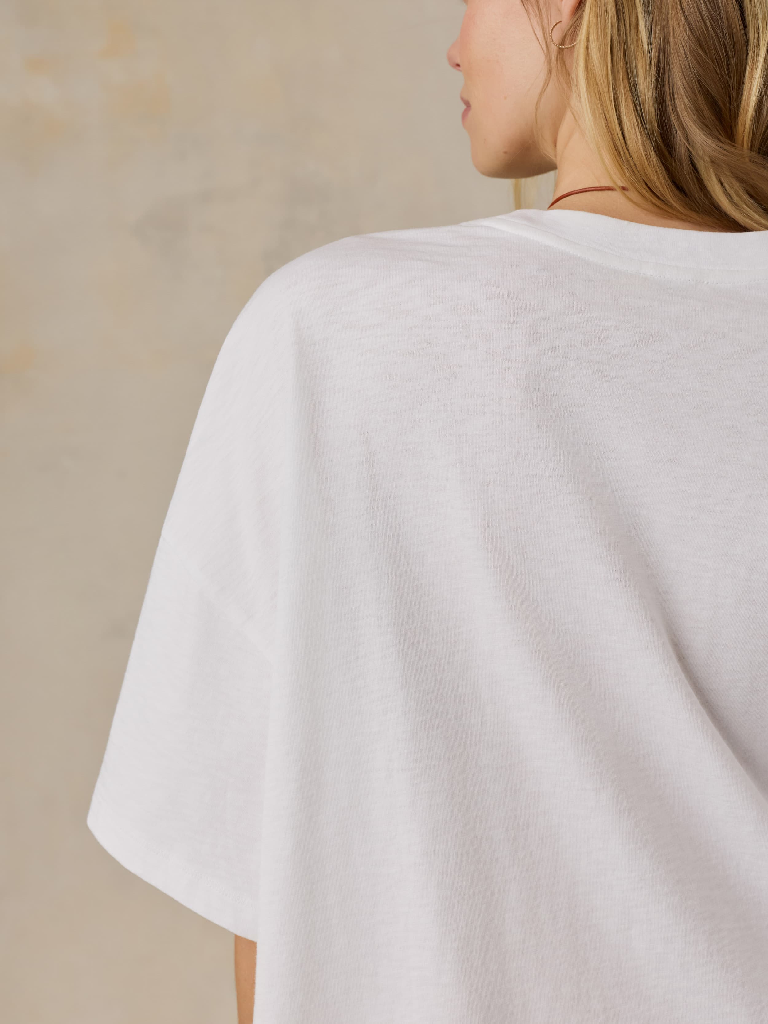 Person wearing a white oversized t-shirt against a beige background