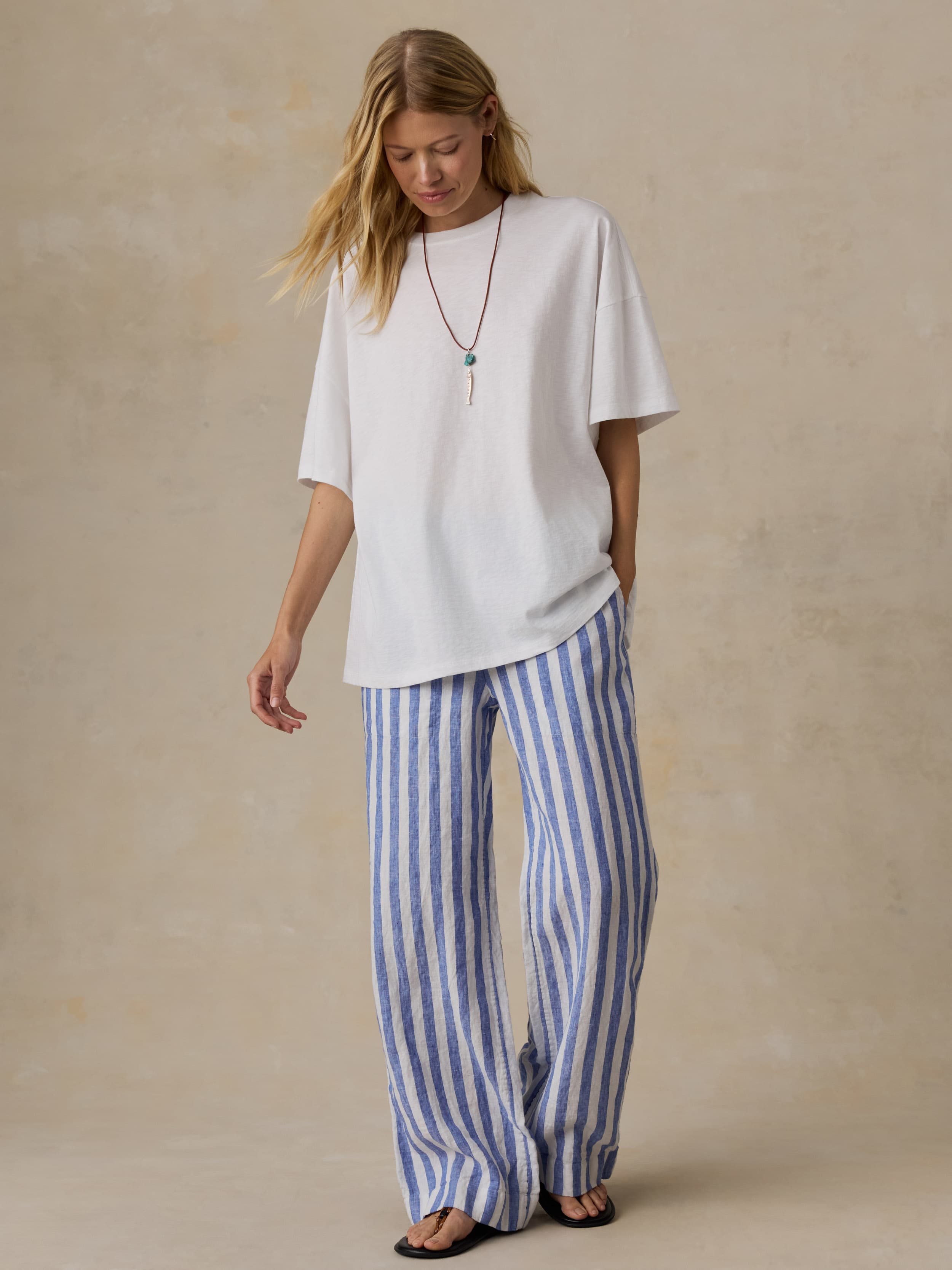 Woman wearing a white oversized t-shirt and blue striped pants against a beige background